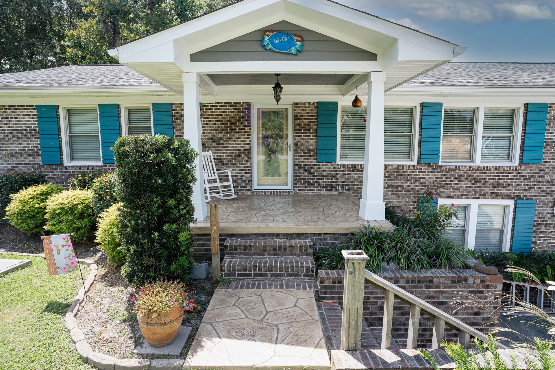 Front view of a brick house with white columns, teal shutters, and a covered porch.