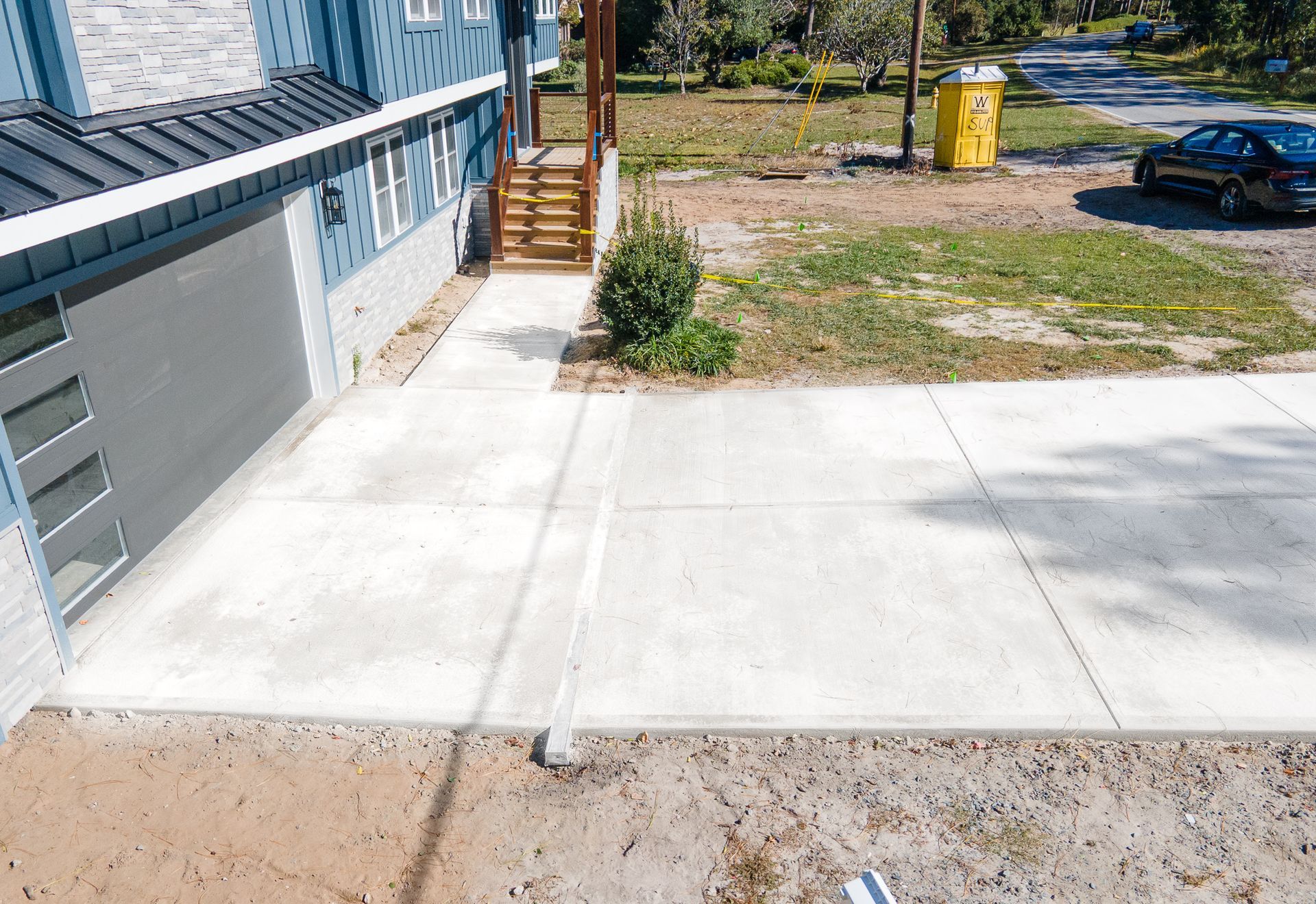 Concrete driveway beside a blue house, with a walkway, stairs, and a parked car in the yard.