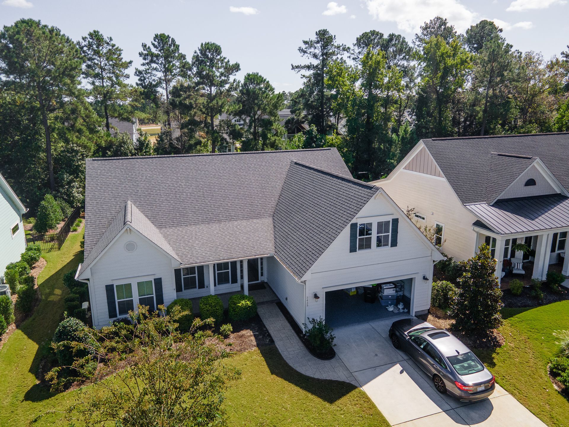 Aerial view of a white suburban house with a gray roof, black garage door, and driveway