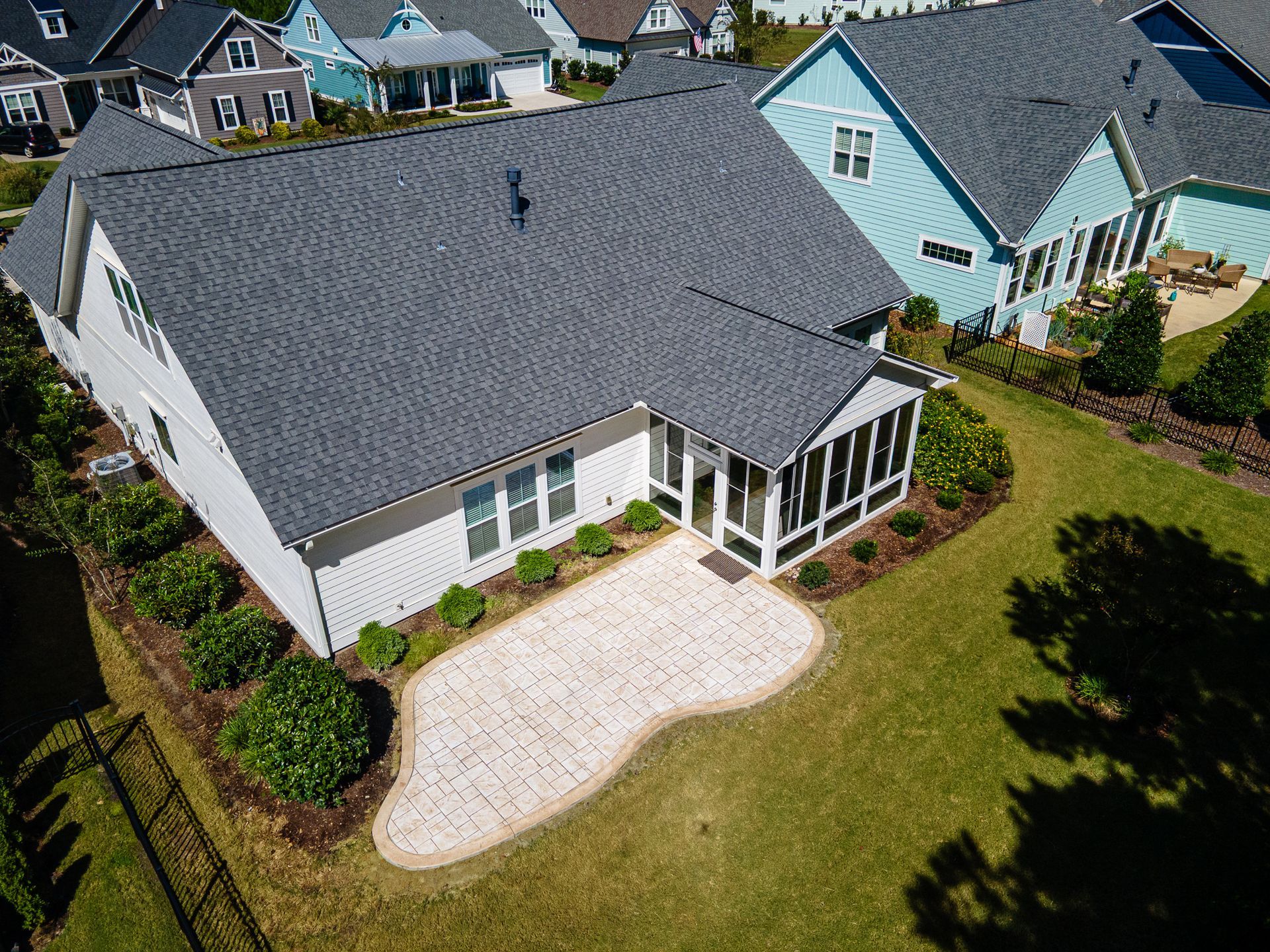 Aerial view of a suburban house with a gray roof, white siding, screened porch, and landscaped yard.