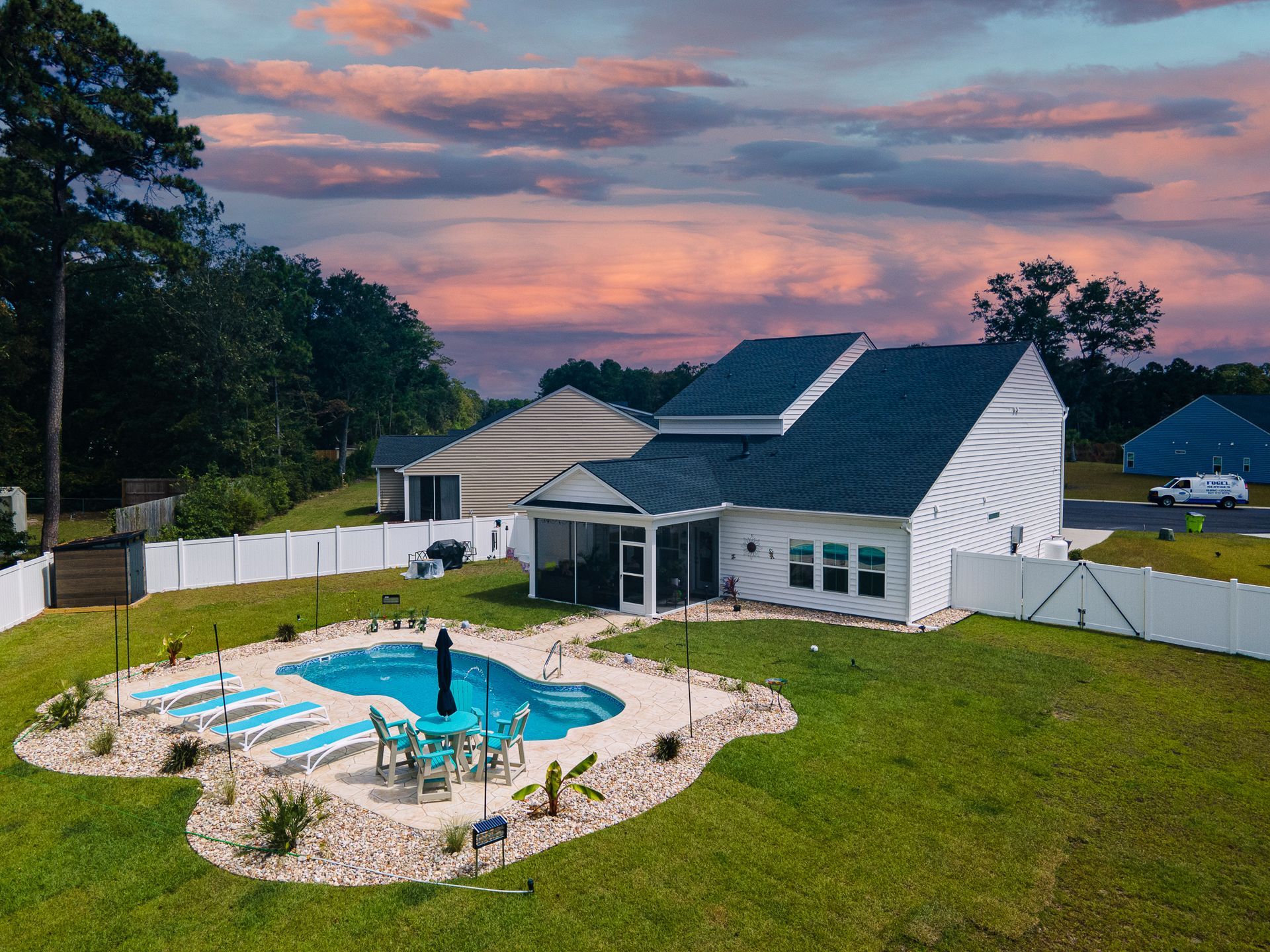 Backyard with a swimming pool, patio chairs, and a white house with solar panels at sunset