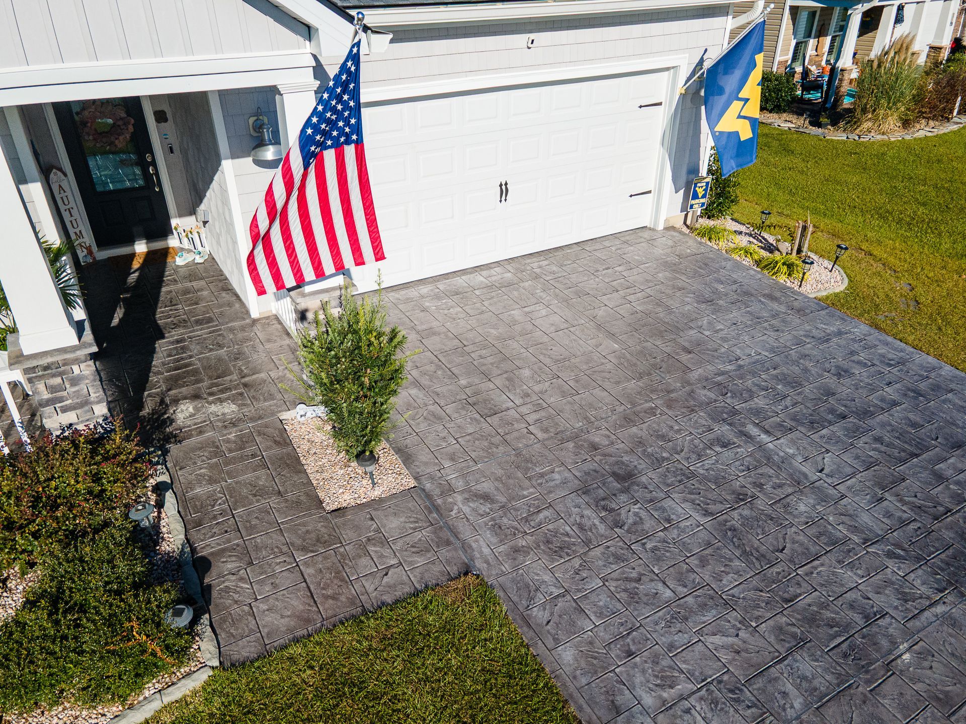 Suburban house front with American and blue-and-yellow flags, gray driveway, and white garage door