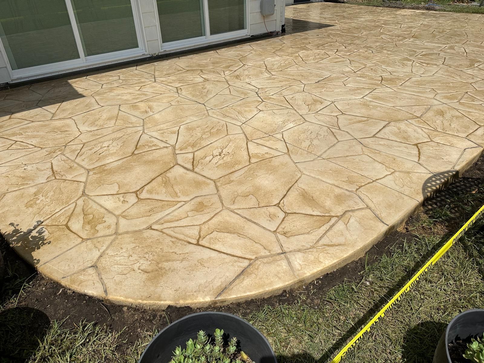 Stamped tan concrete patio beside a house, with a curved edge and garden border.
