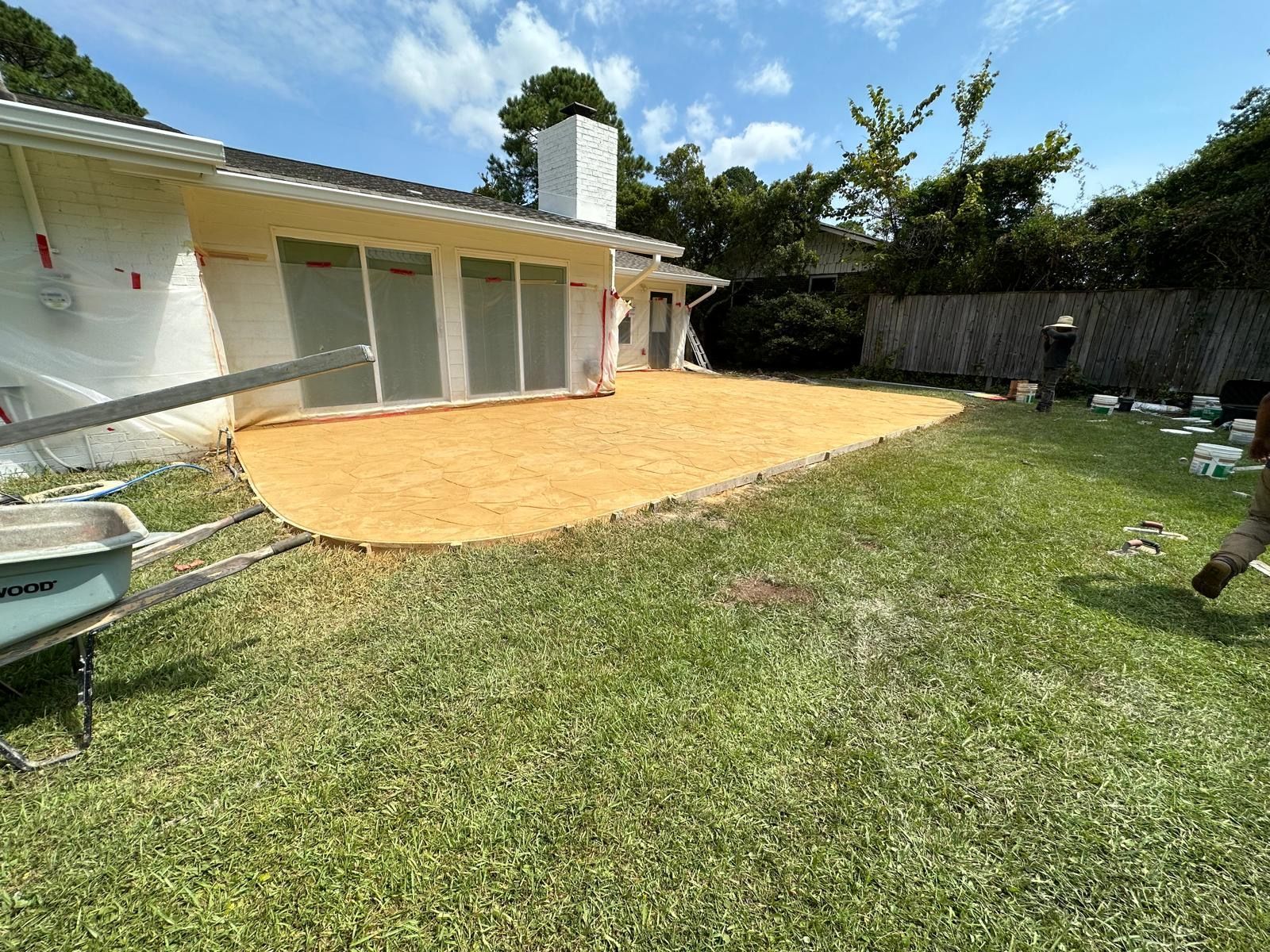 Backyard with a patio, lawn, and a white house under a sunny sky