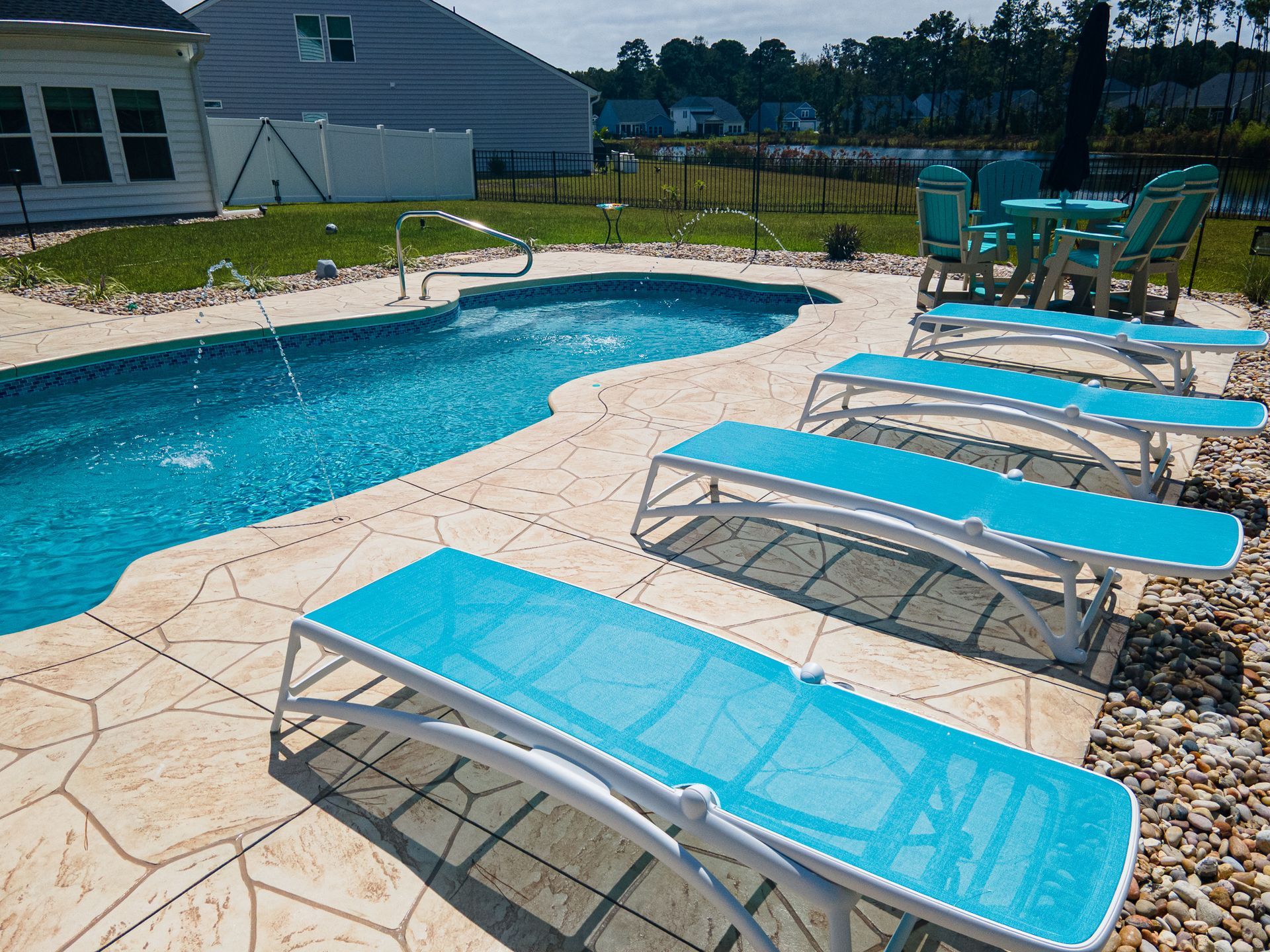 Backyard pool with turquoise lounge chairs on a stone patio and a house in the background
