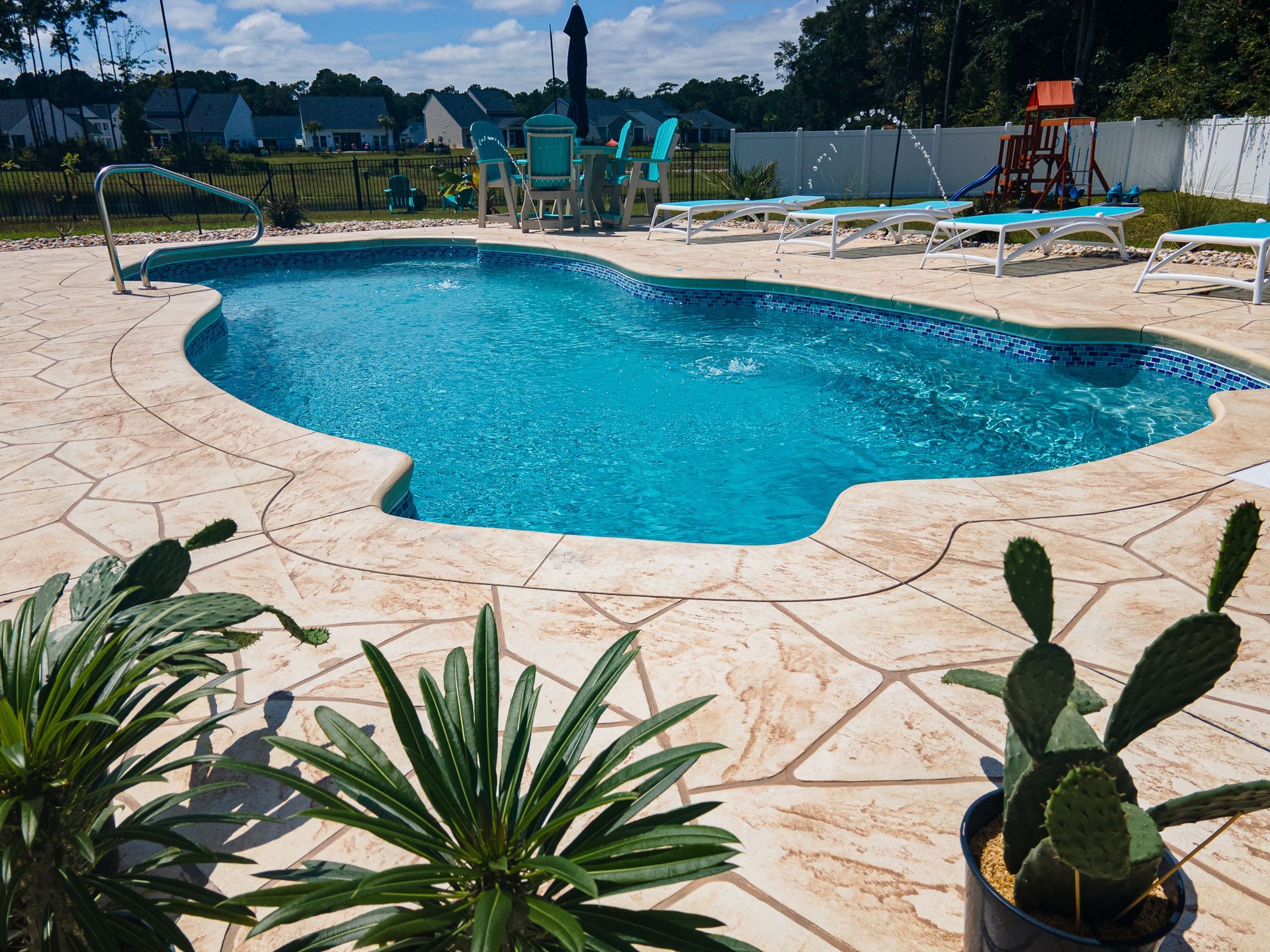 Backyard swimming pool with turquoise water, stone patio, and potted plants in the foreground