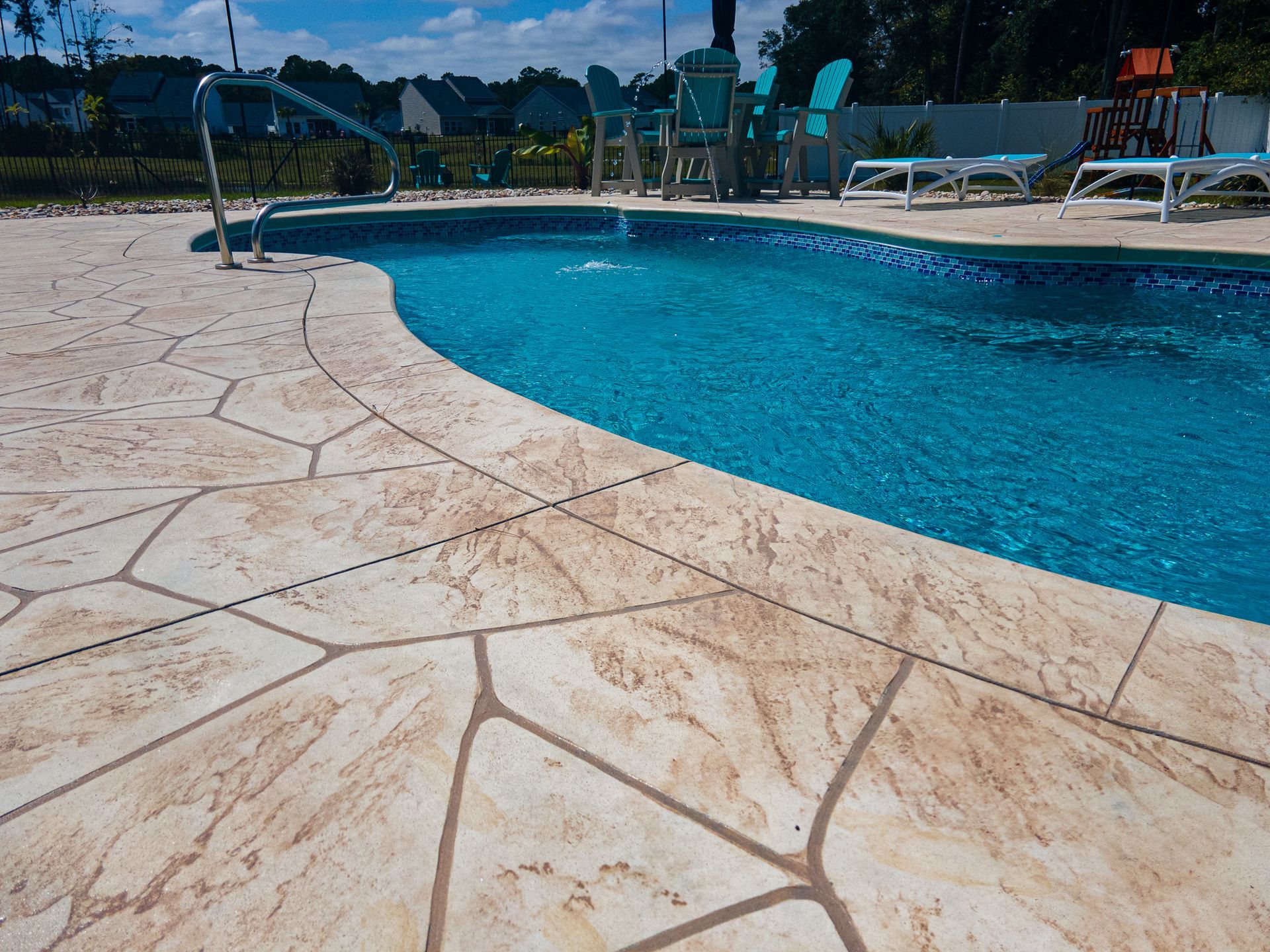 Outdoor swimming pool with blue water and tan stone deck, lounge chairs in the background