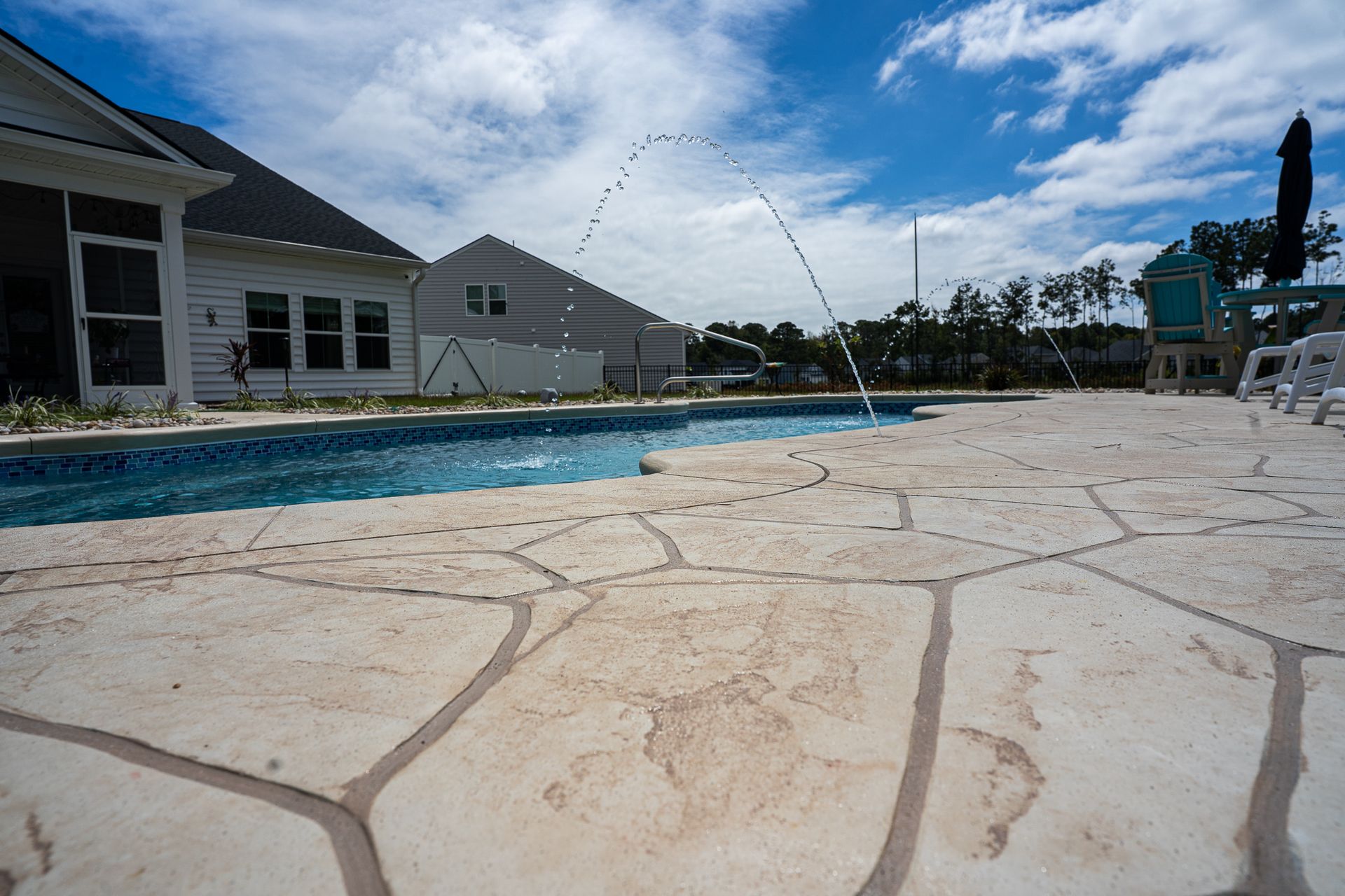 Stone pool deck beside a backyard swimming pool and house under a blue sky