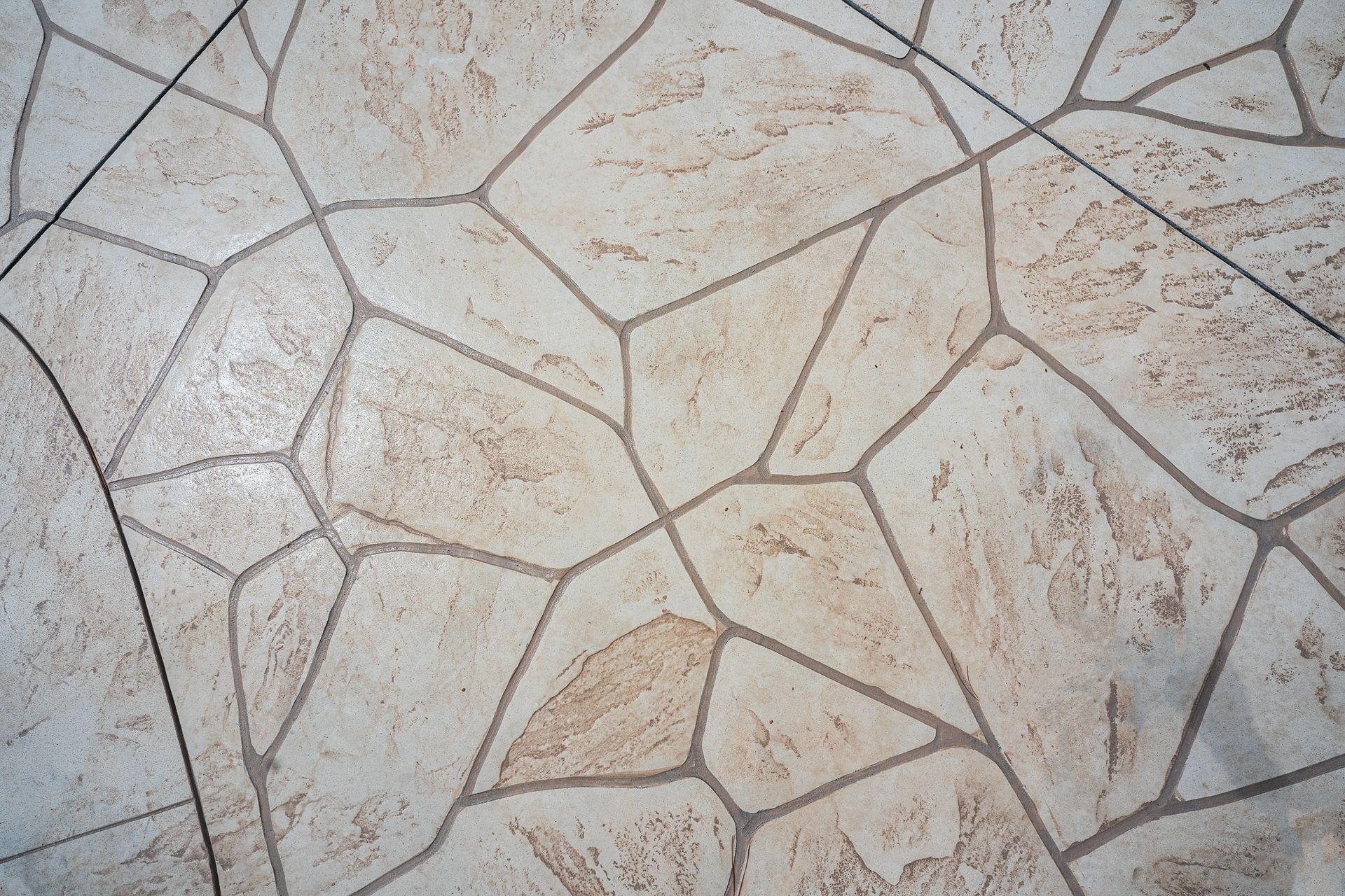 Close-up of light beige irregular stone tiles with gray grout lines and subtle brown stains