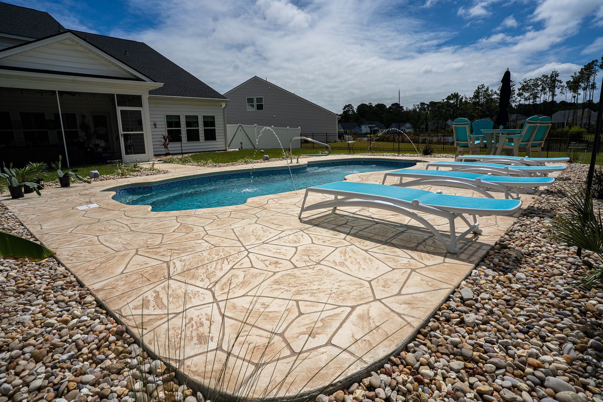 Outdoor swimming pool with blue lounge chairs and a stone patio beside a house