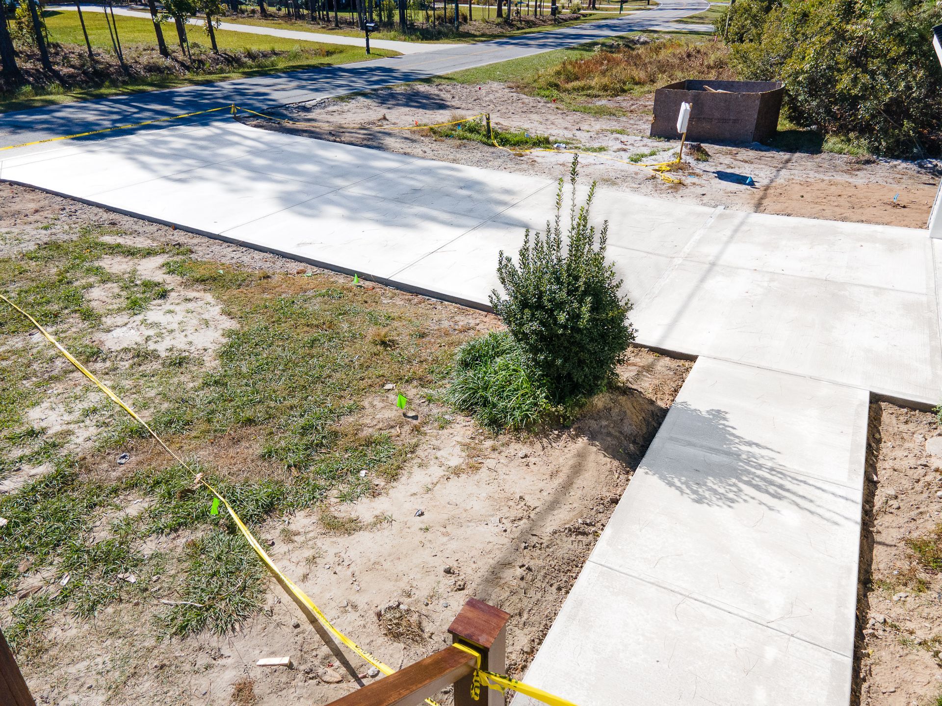 Concrete driveway beside a dirt lot with a small shrub and yellow tape marking the ground