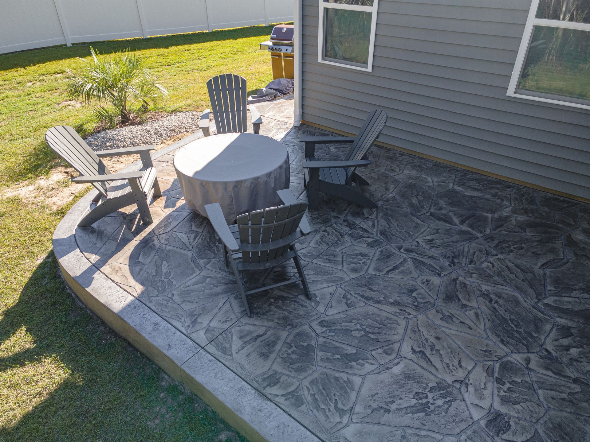 Patio with round table and four chairs on stamped concrete beside a gray house