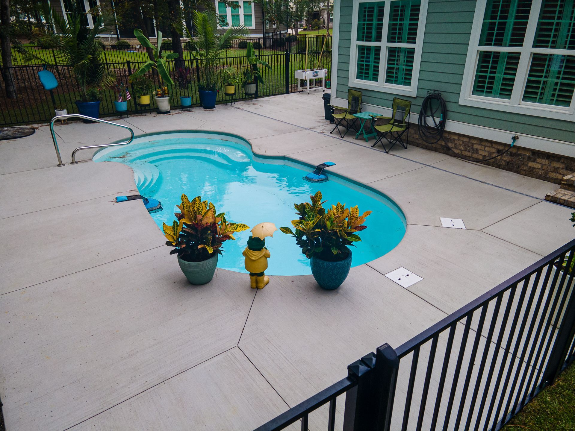 Backyard pool with turquoise water, potted flowers, and a black fence beside a brick house