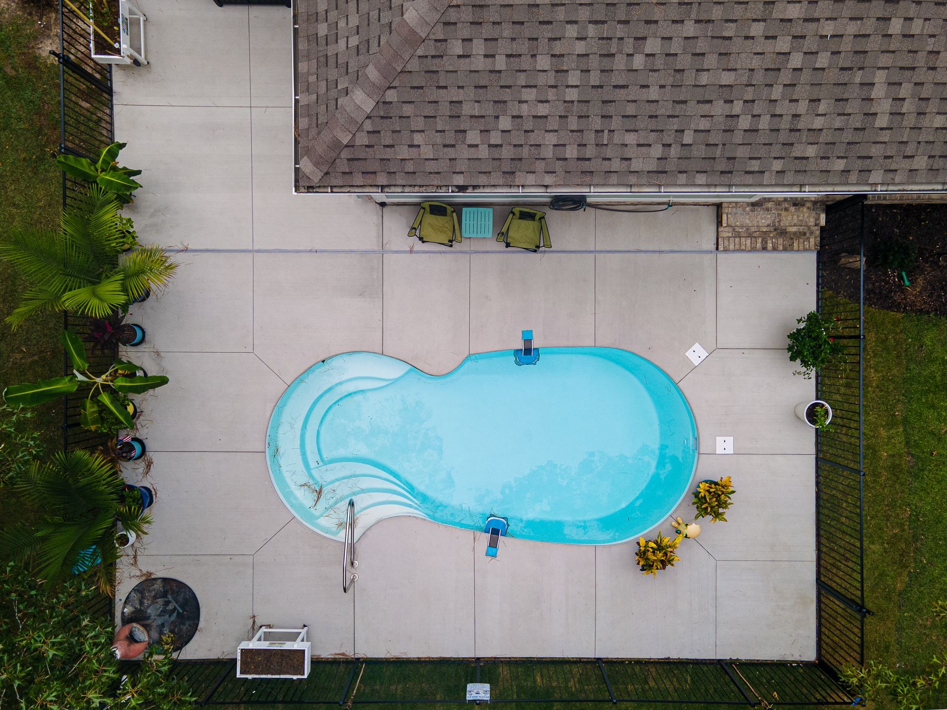Aerial view of a backyard with a turquoise swimming pool beside a patio and house roof.