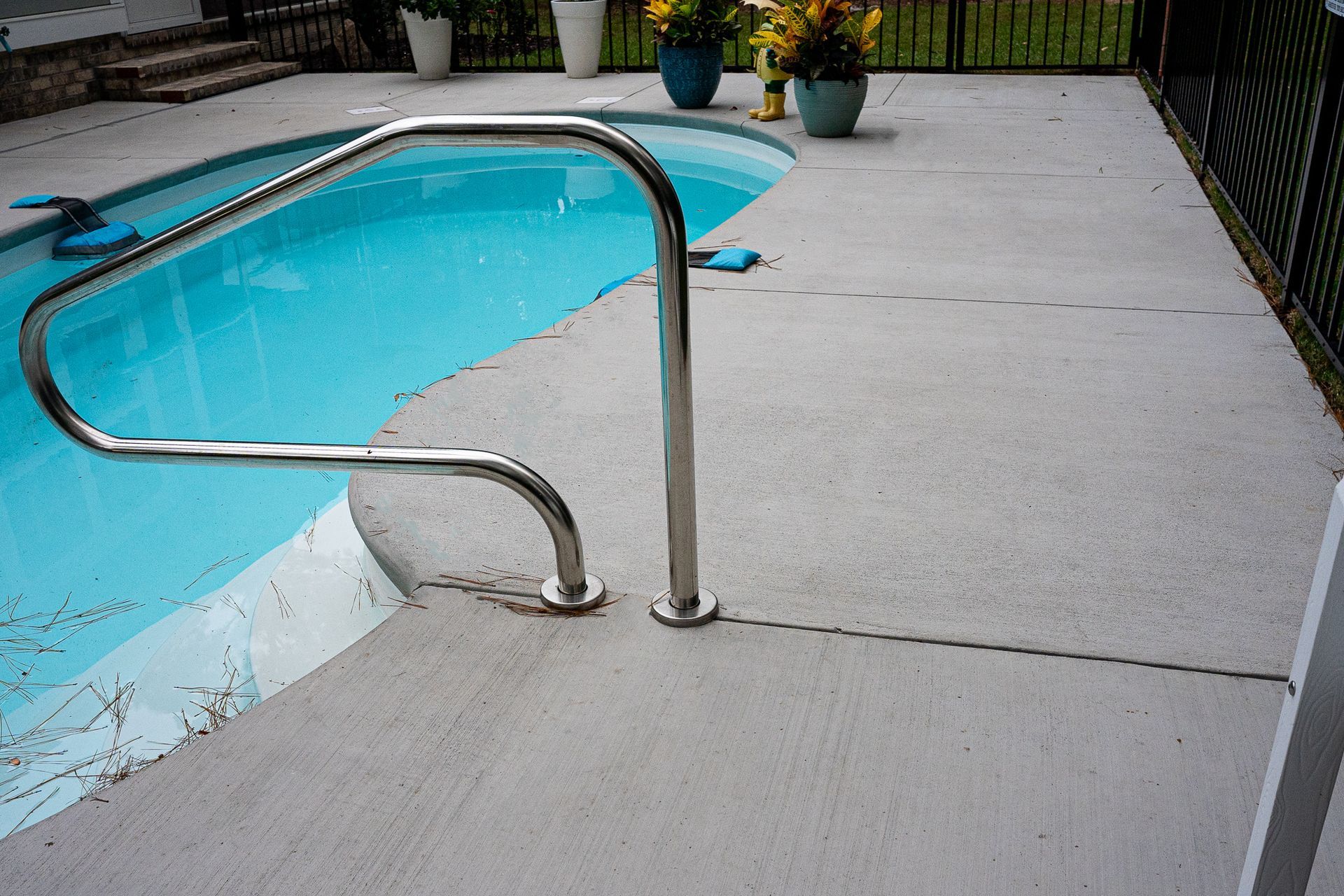 Poolside concrete deck with stainless steel handrails beside a turquoise swimming pool