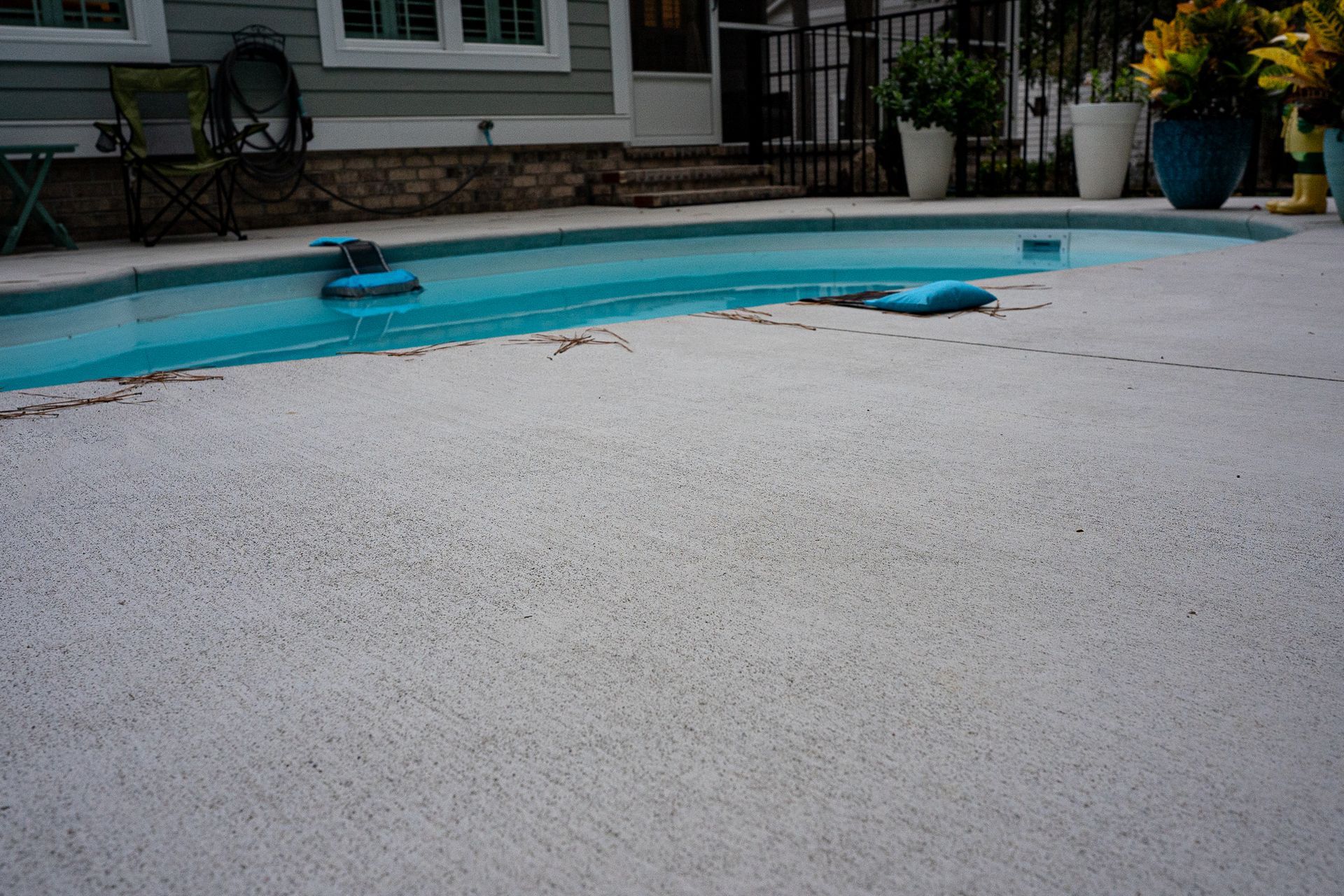 Empty turquoise swimming pool with a rough white coating in a backyard patio area