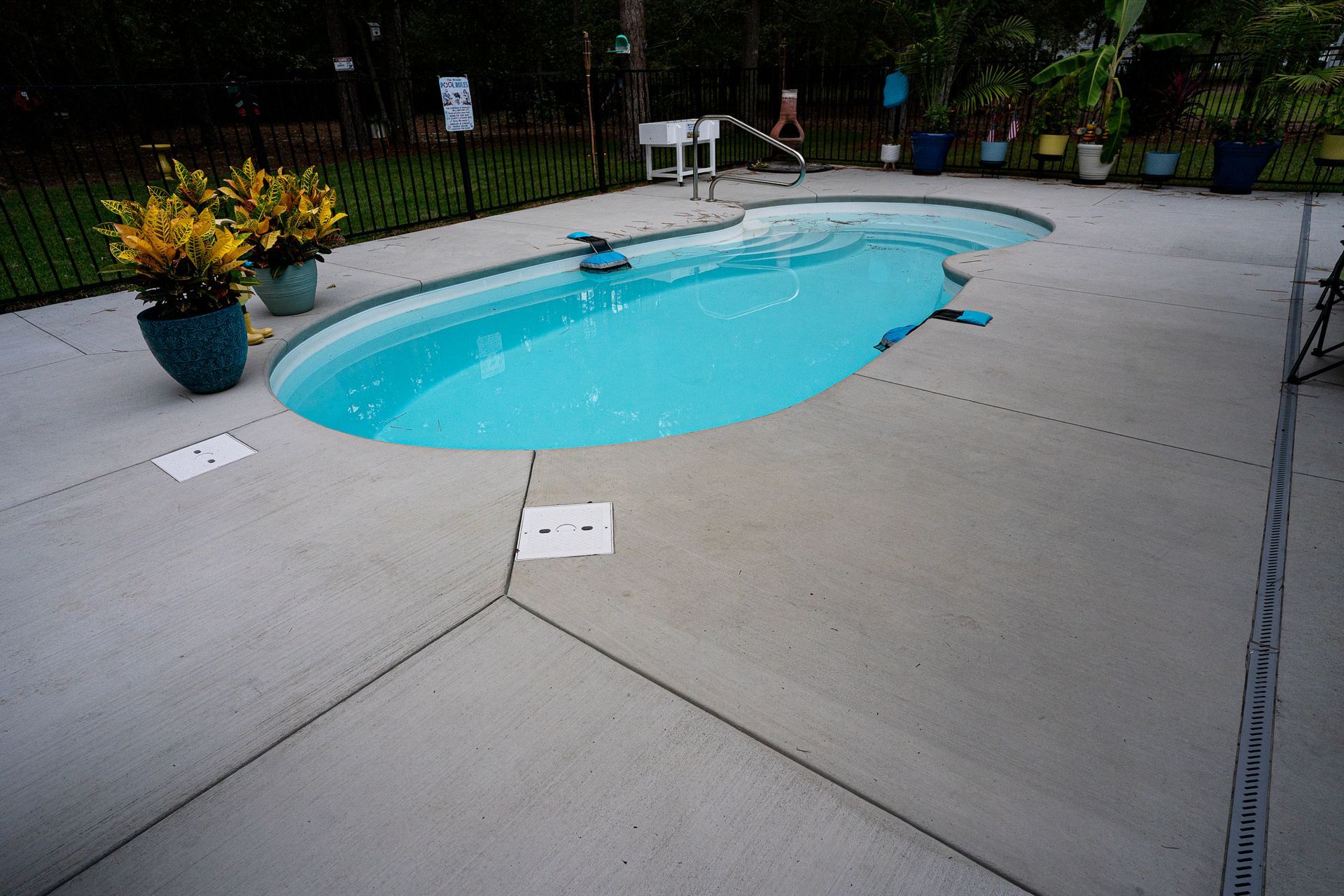 Backyard swimming pool with bright blue water and concrete deck, surrounded by potted plants and a fence