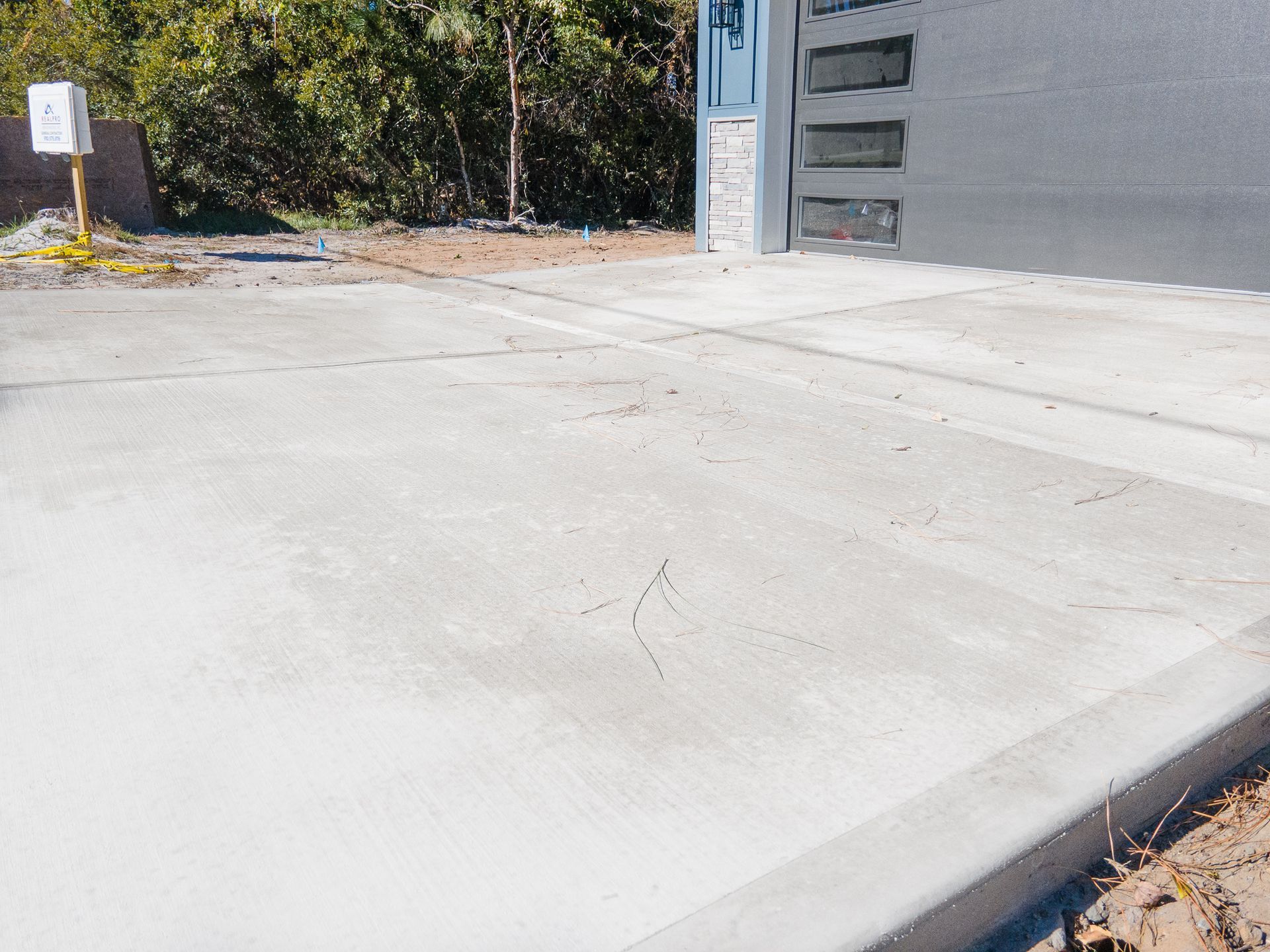 Concrete driveway leading to a gray garage beside trees and bushes