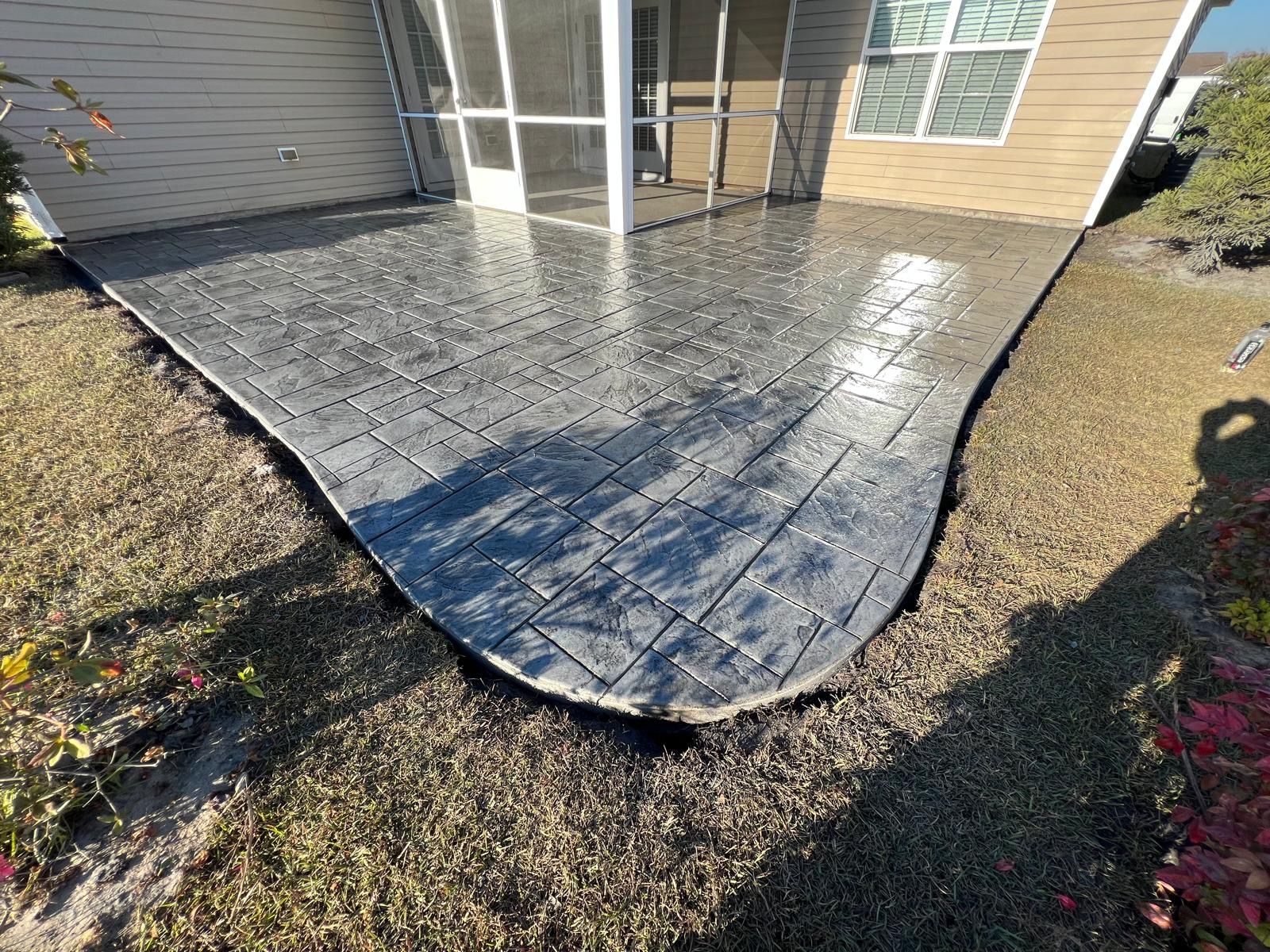 Curved stone patio beside a house, with screened doors and dry grass along the edge.