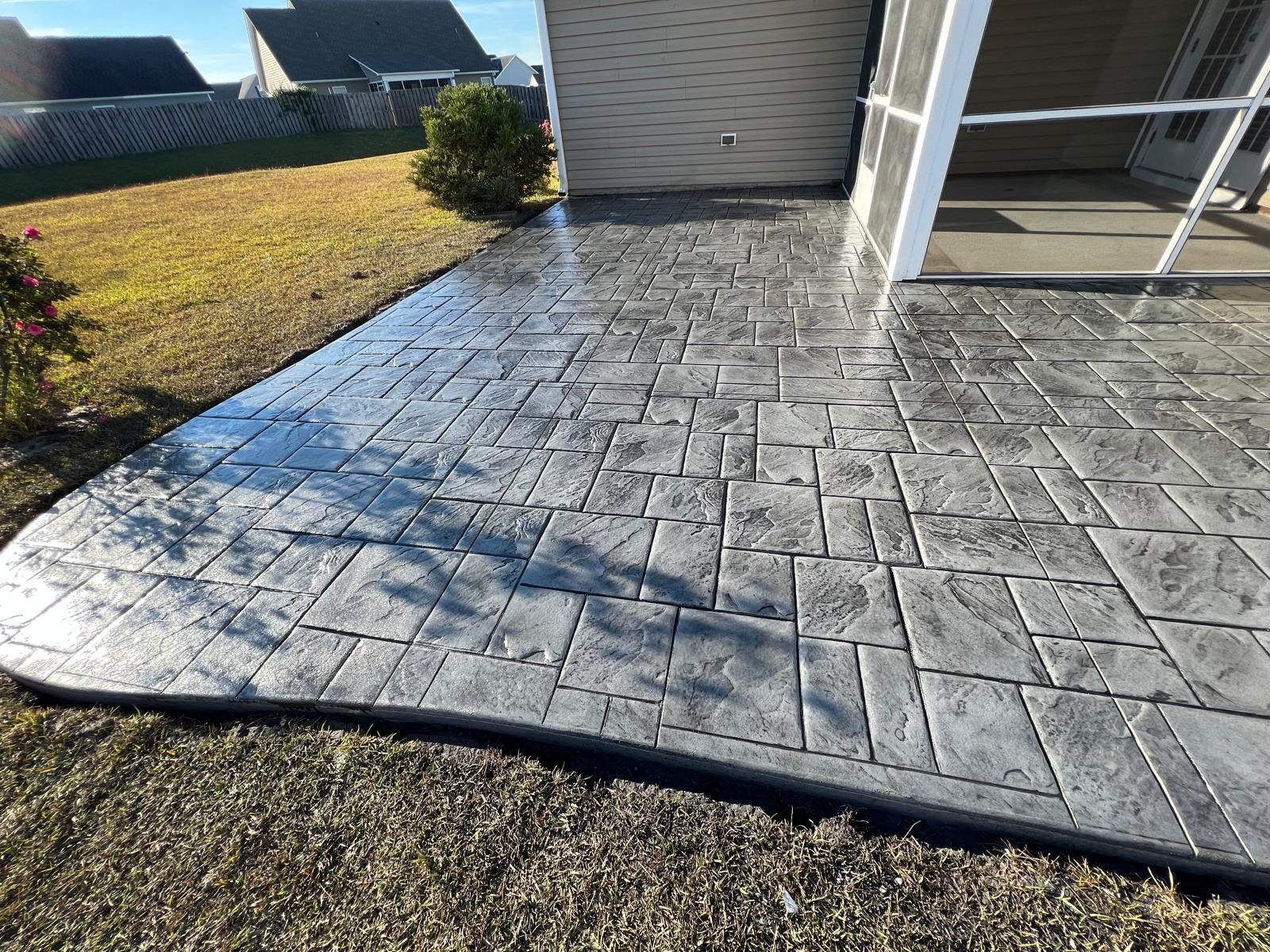 Stamped concrete patio beside a house, with a stone pattern and adjacent lawn