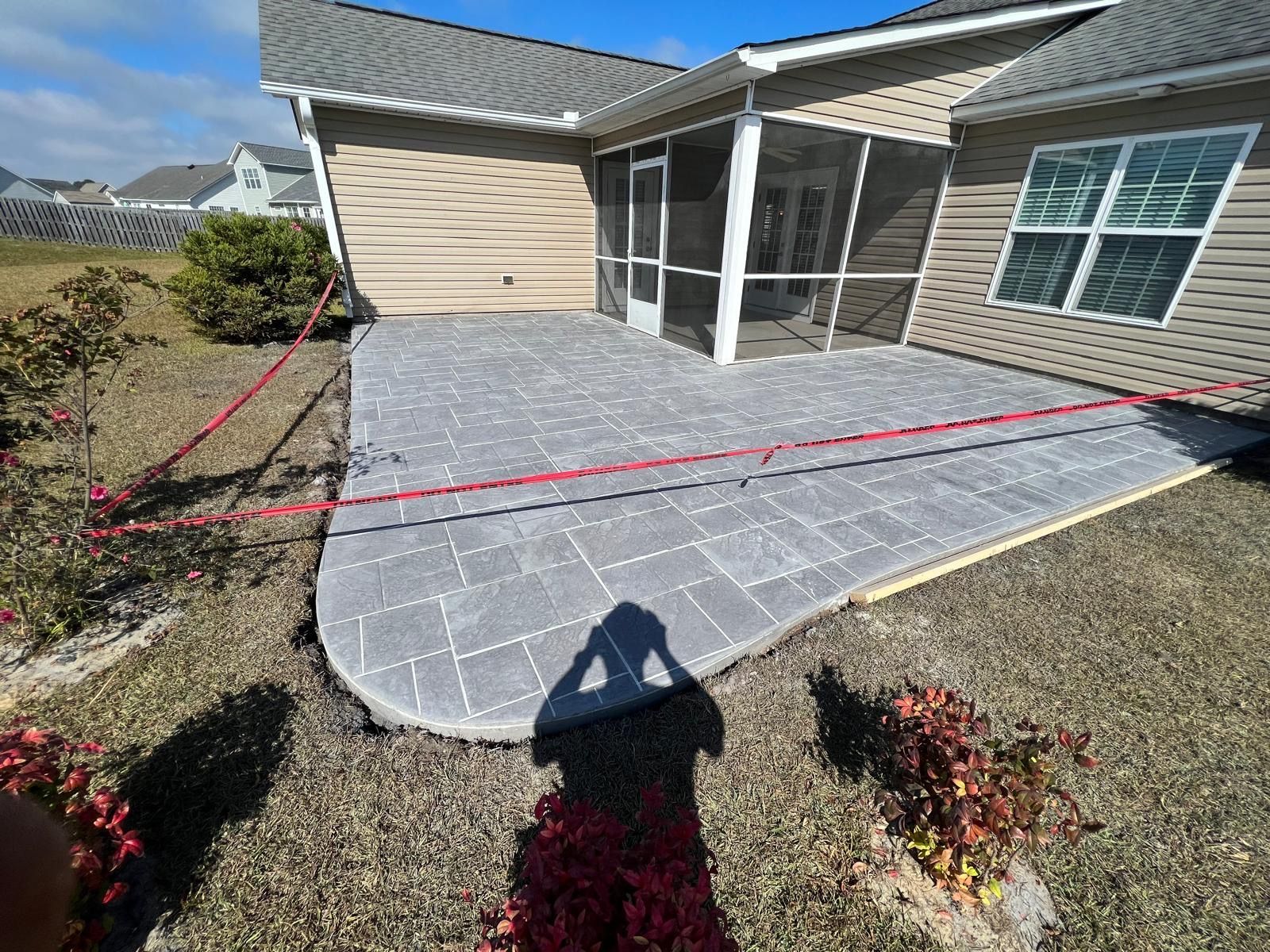 Backyard patio with gray pavers and red string line beside a beige house and screened porch