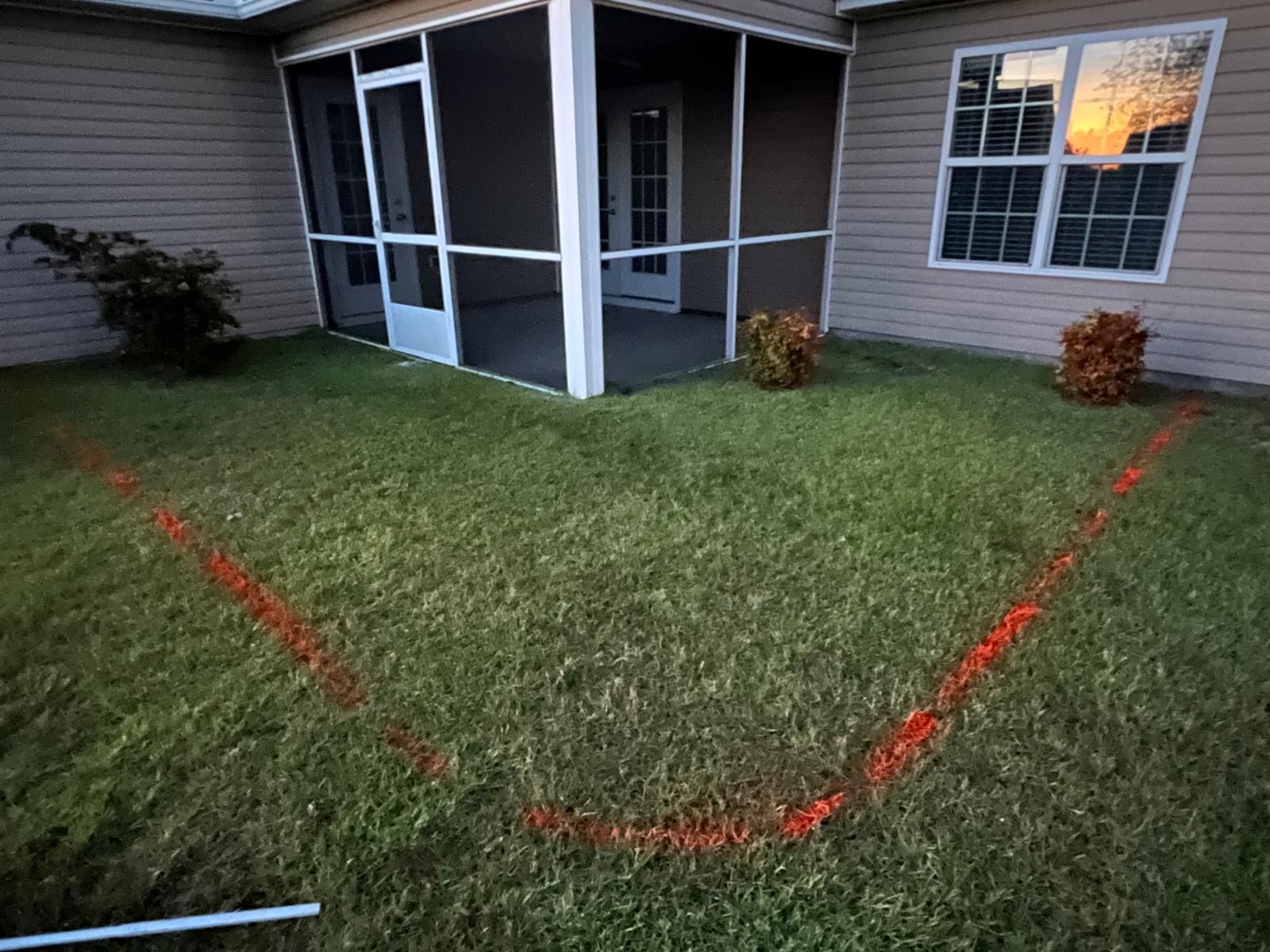 Red spray-painted outline marks a section of lawn beside a screened porch and house window.