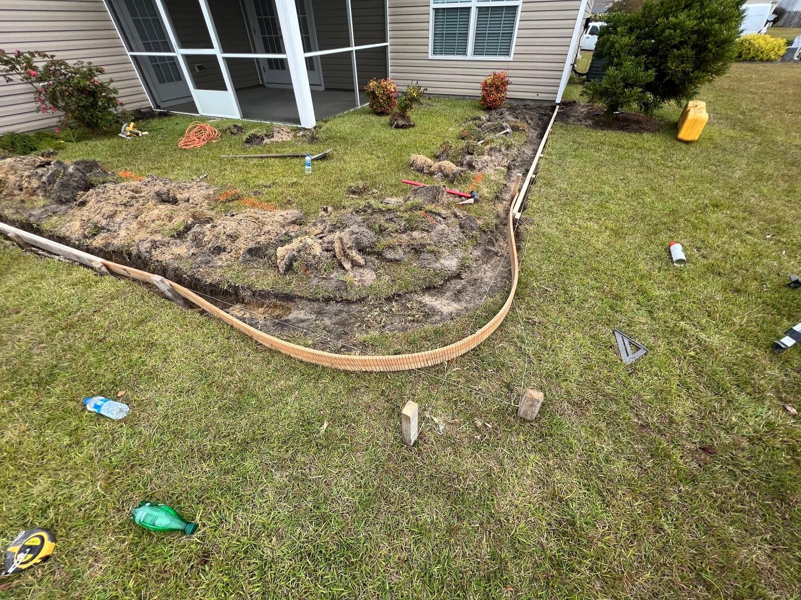 Front yard with damaged mulch border and patchy grass beside a house, with scattered litter on the lawn.