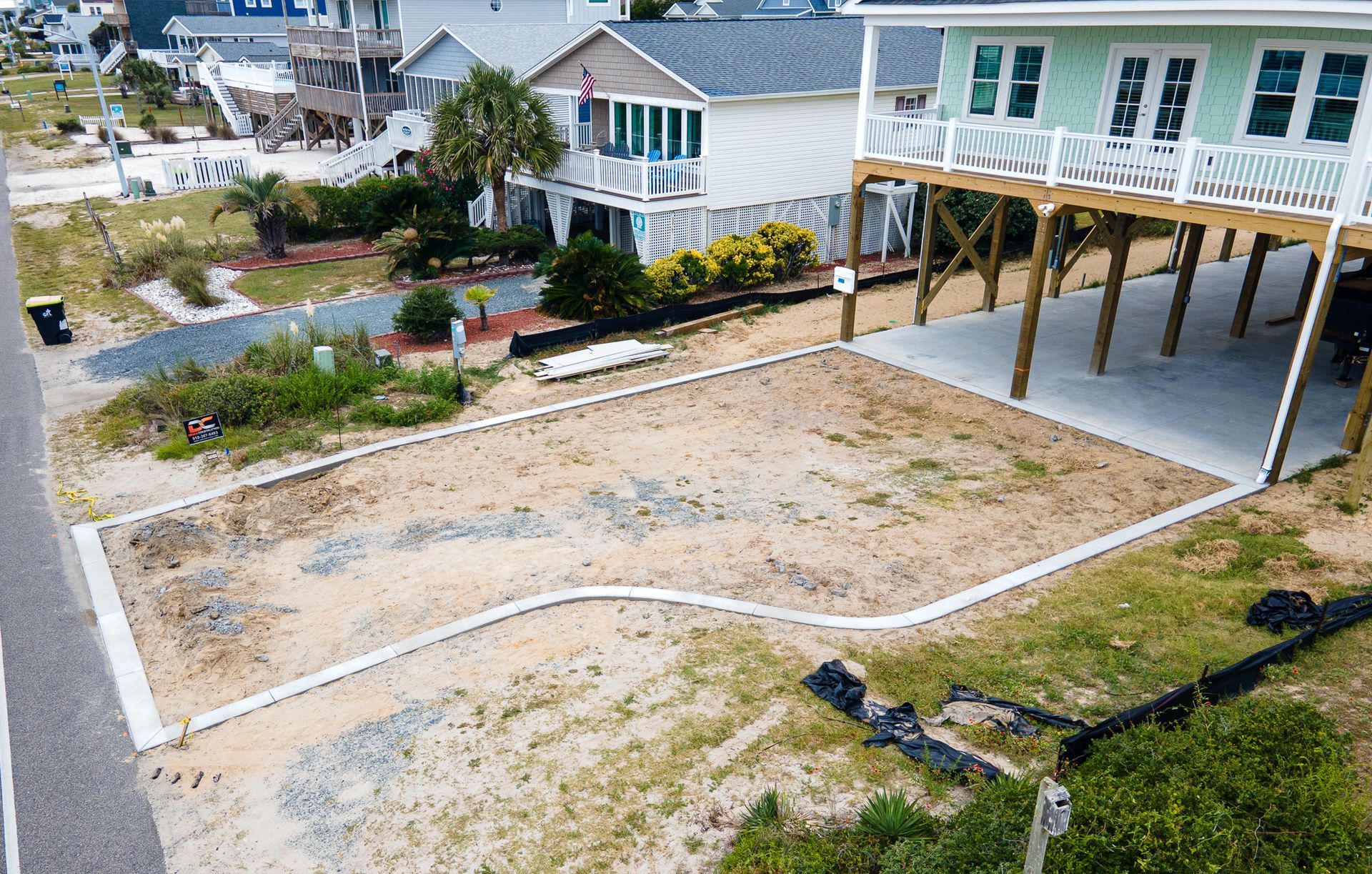 Flood-damaged yard beside a raised house, with exposed sandy ground and scattered debris.