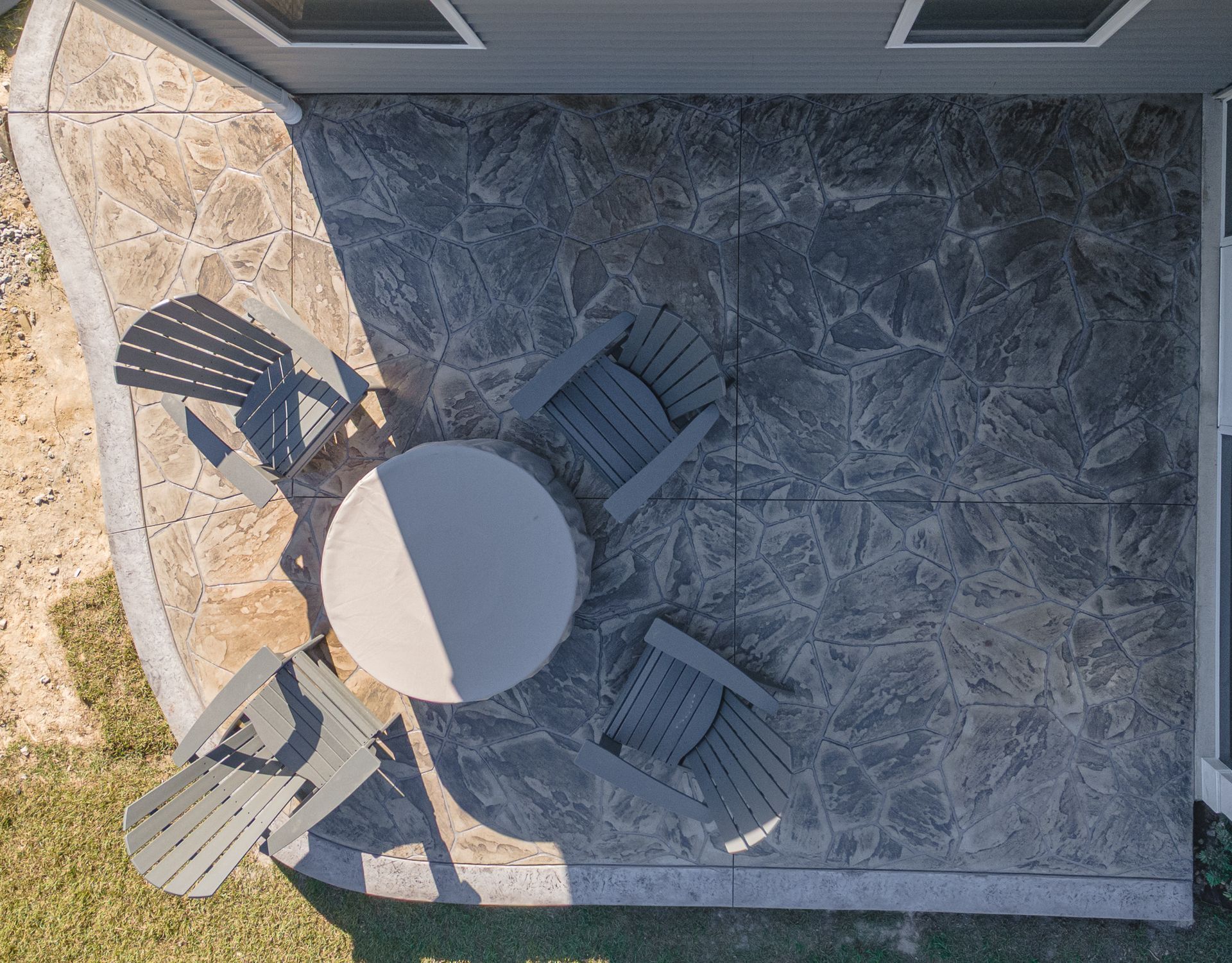 Overhead view of a stone patio with a round table and four chairs, beside a grassy lawn.
