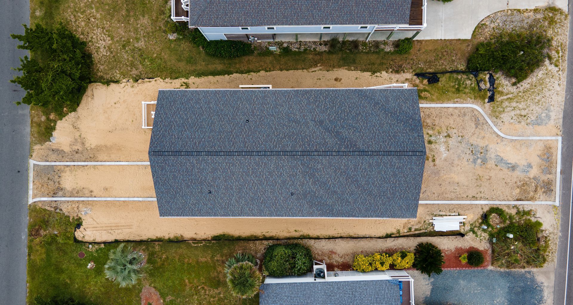 Aerial view of a gray-roofed house with beige gravel yard and surrounding desert landscaping.