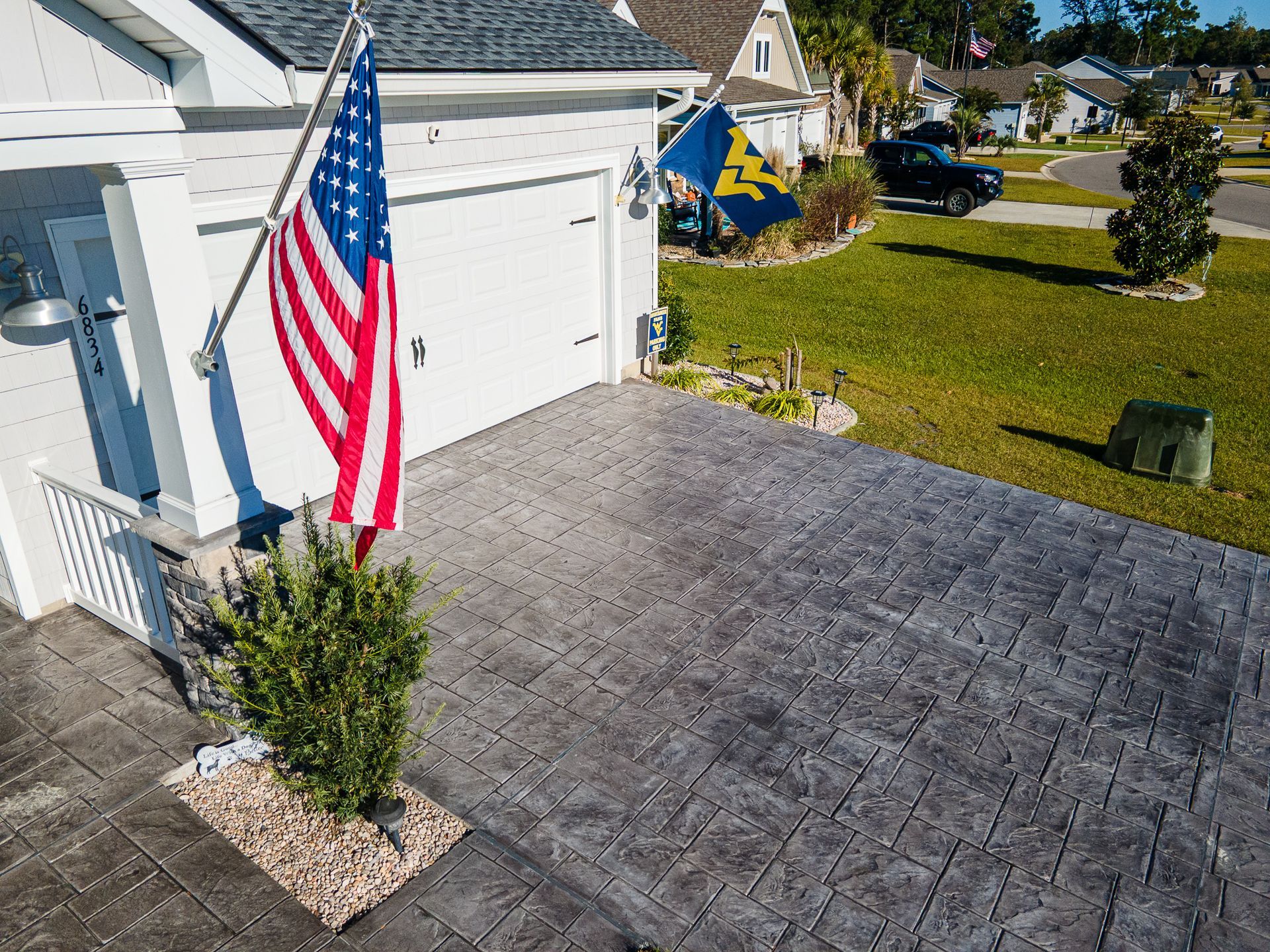 Front yard with an American flag, paved driveway, garage, and suburban houses in sunlight