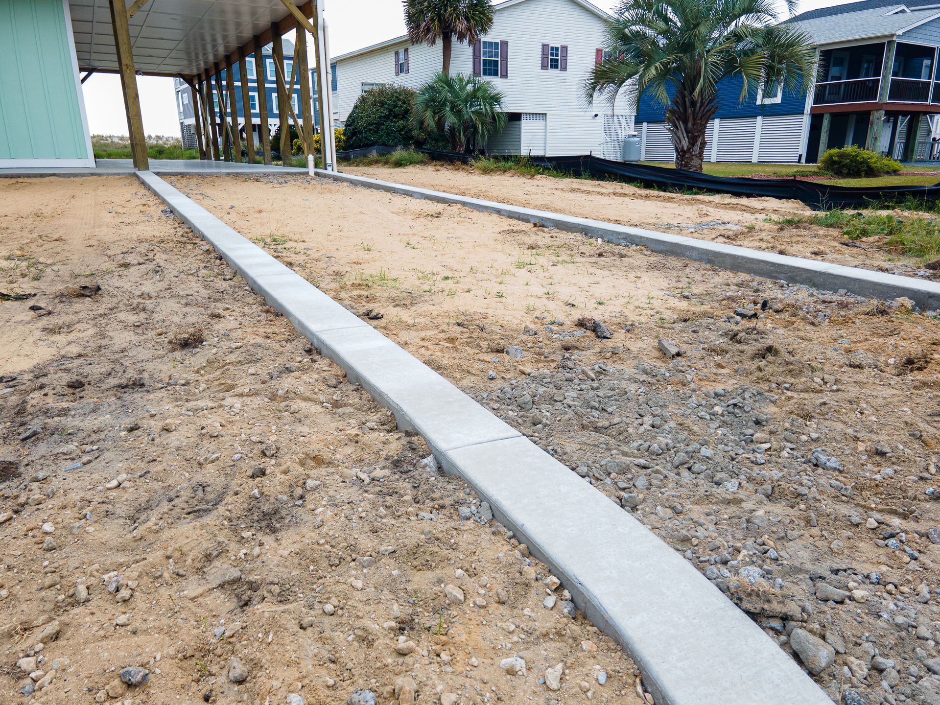 New concrete walkway between two sandy lots beside white houses and palm trees