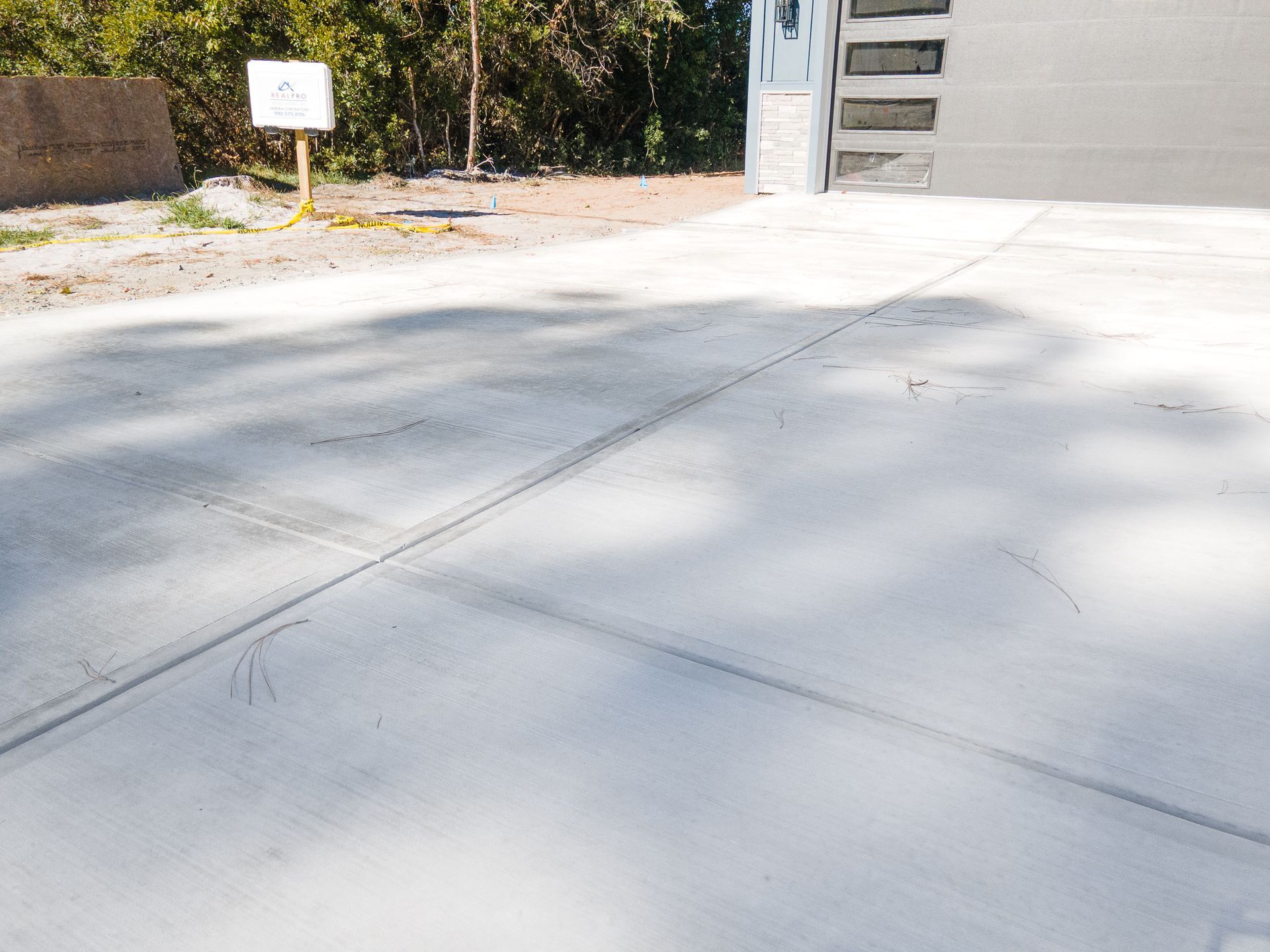 Empty concrete driveway beside a garage, with a small sign near the curb.