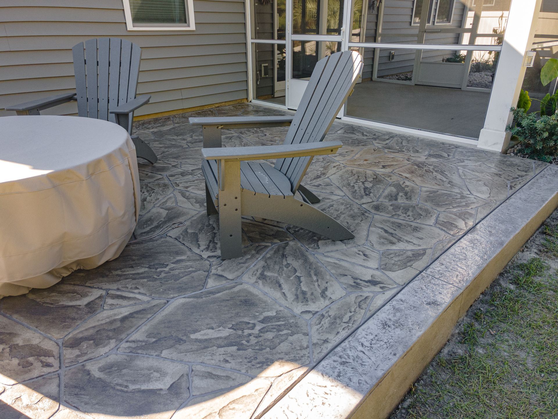 Patio with two Adirondack chairs on a patterned outdoor rug beside a covered table and house siding