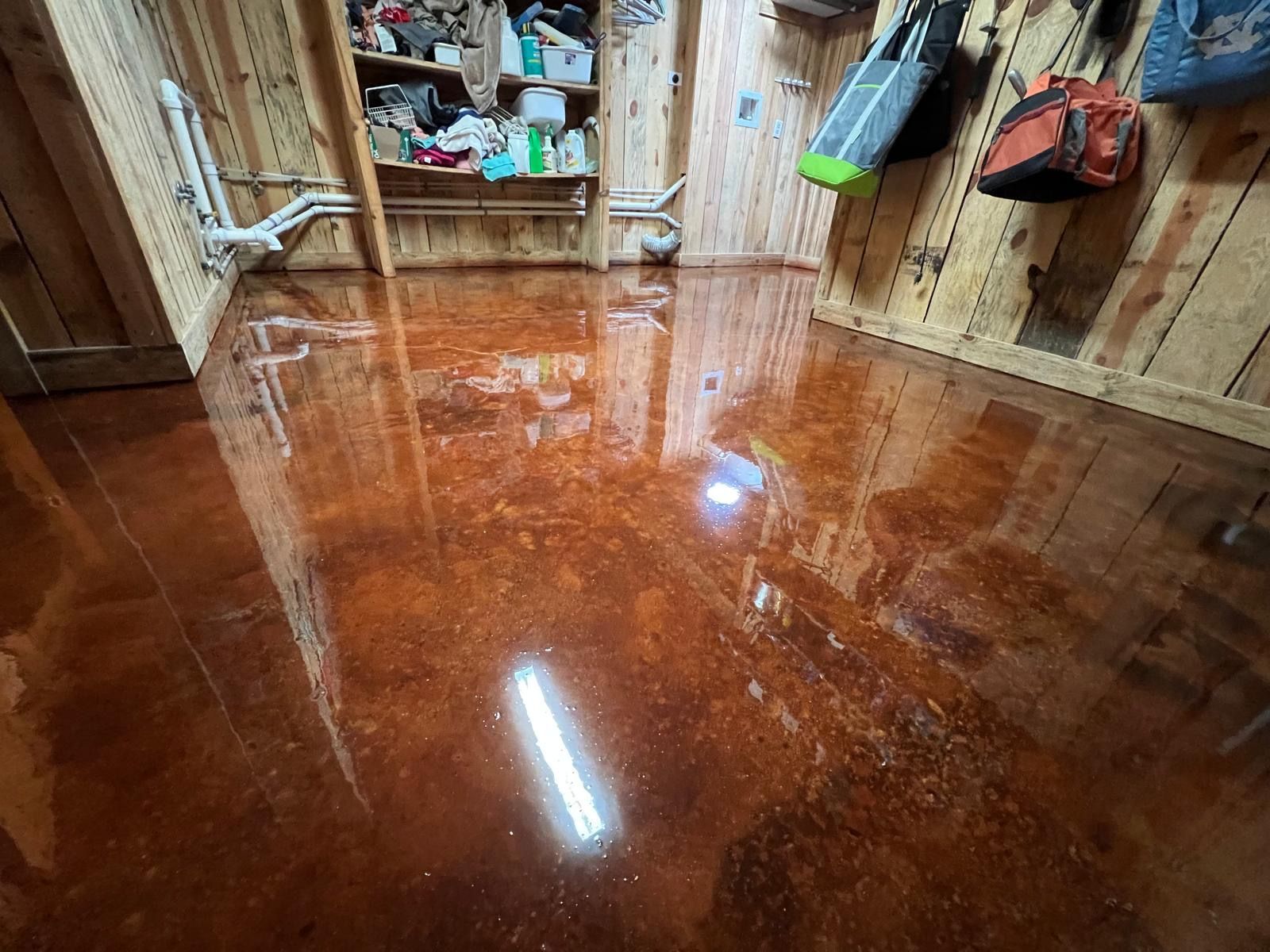 Flooded basement with glossy water covering the floor and storage shelves along the walls