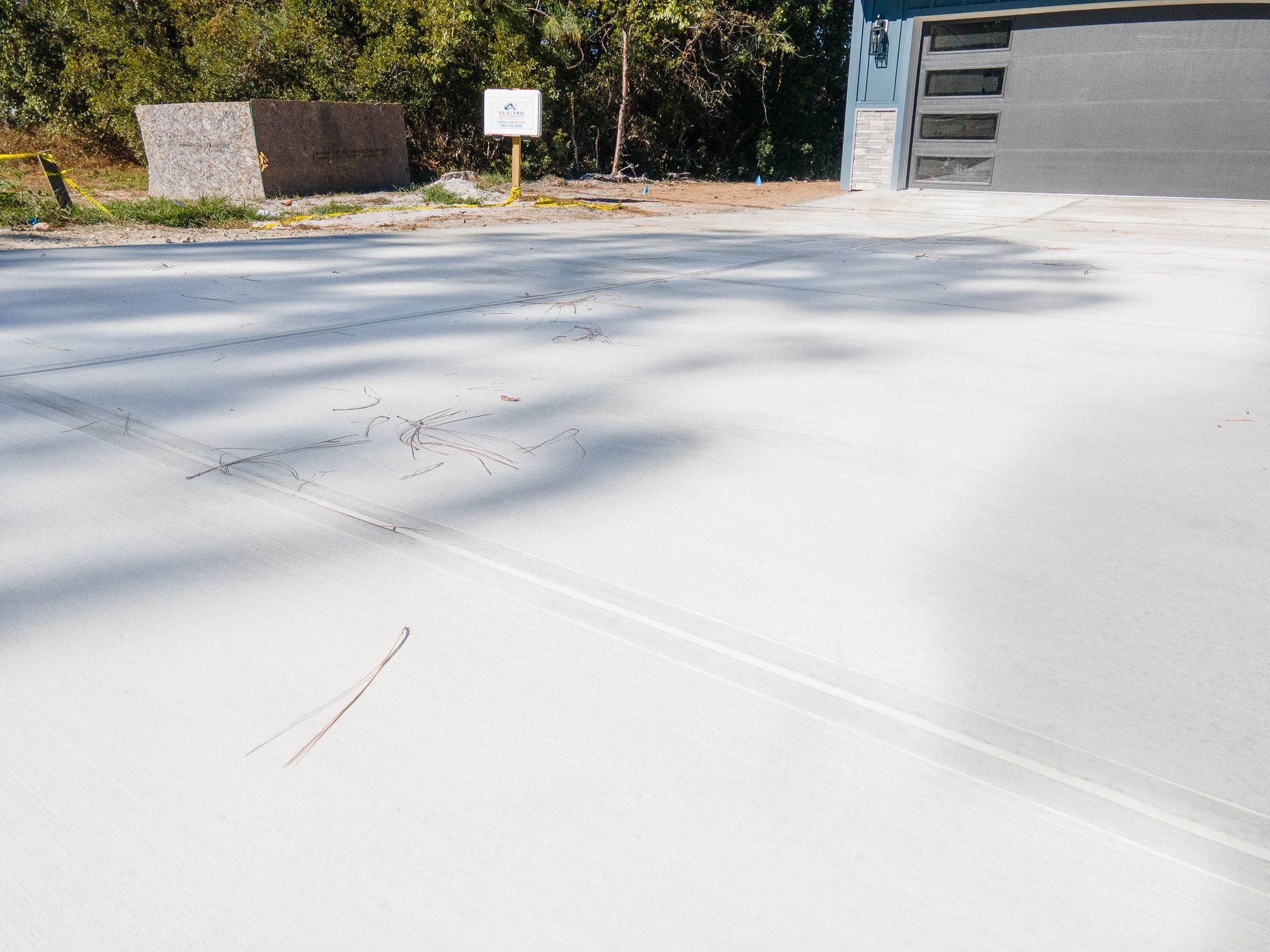 Sunny paved driveway with a garage, small sign, and trees in the background