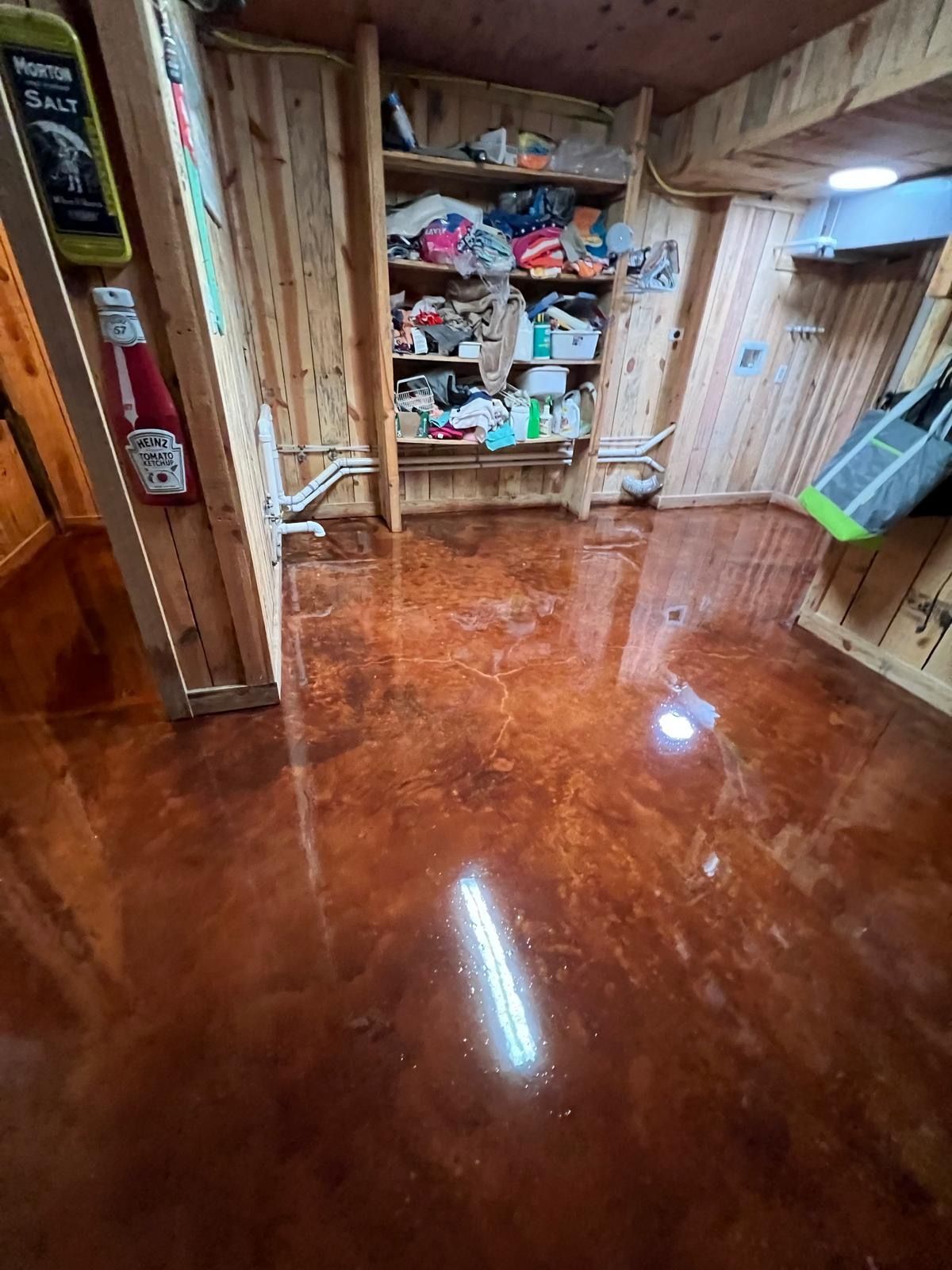 Glossy brown floor in a wood-paneled room with a cluttered shelf and cleaning tools