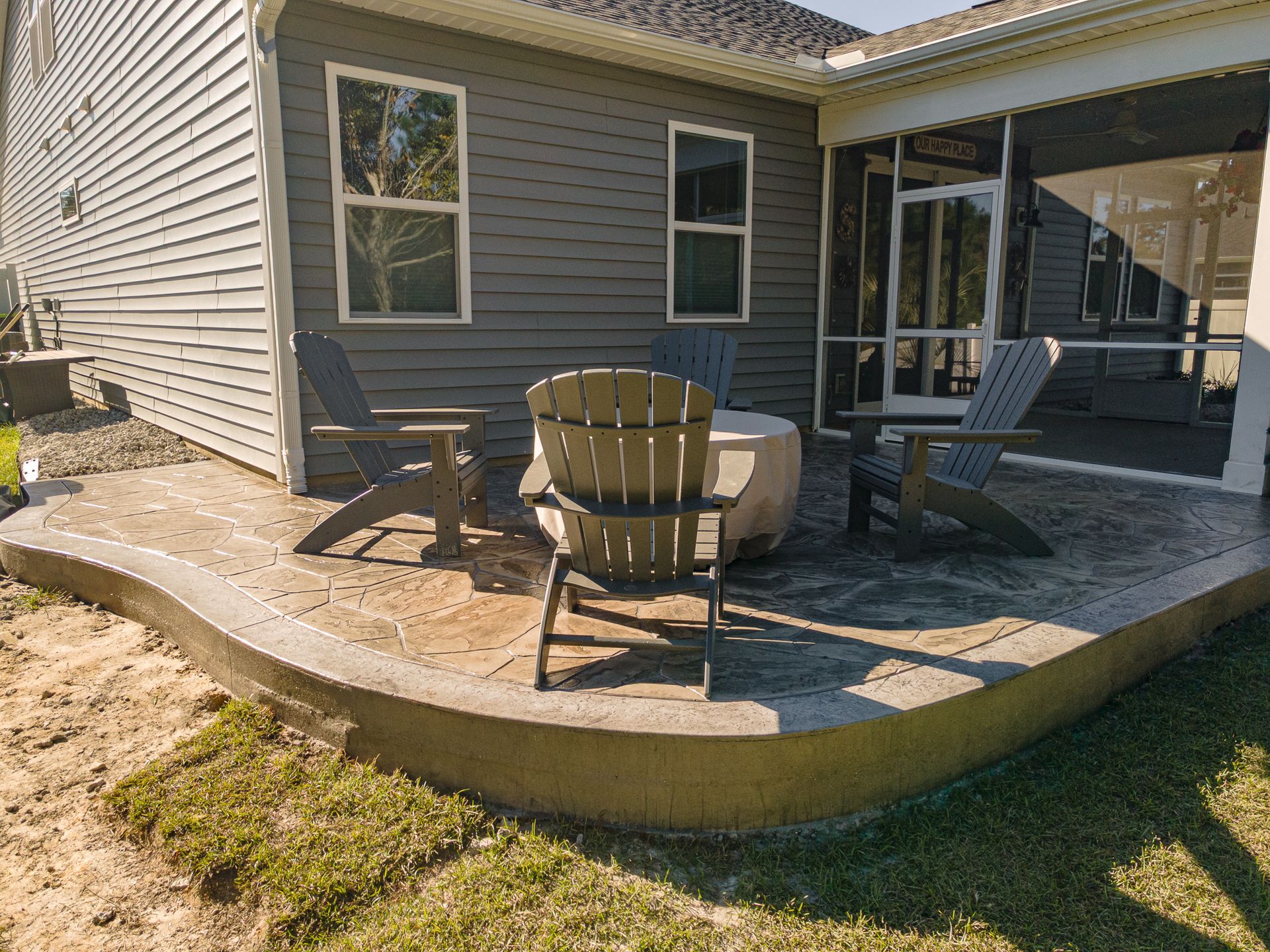 Patio with Adirondack chairs beside a house’s screened porch and stone paver patio
