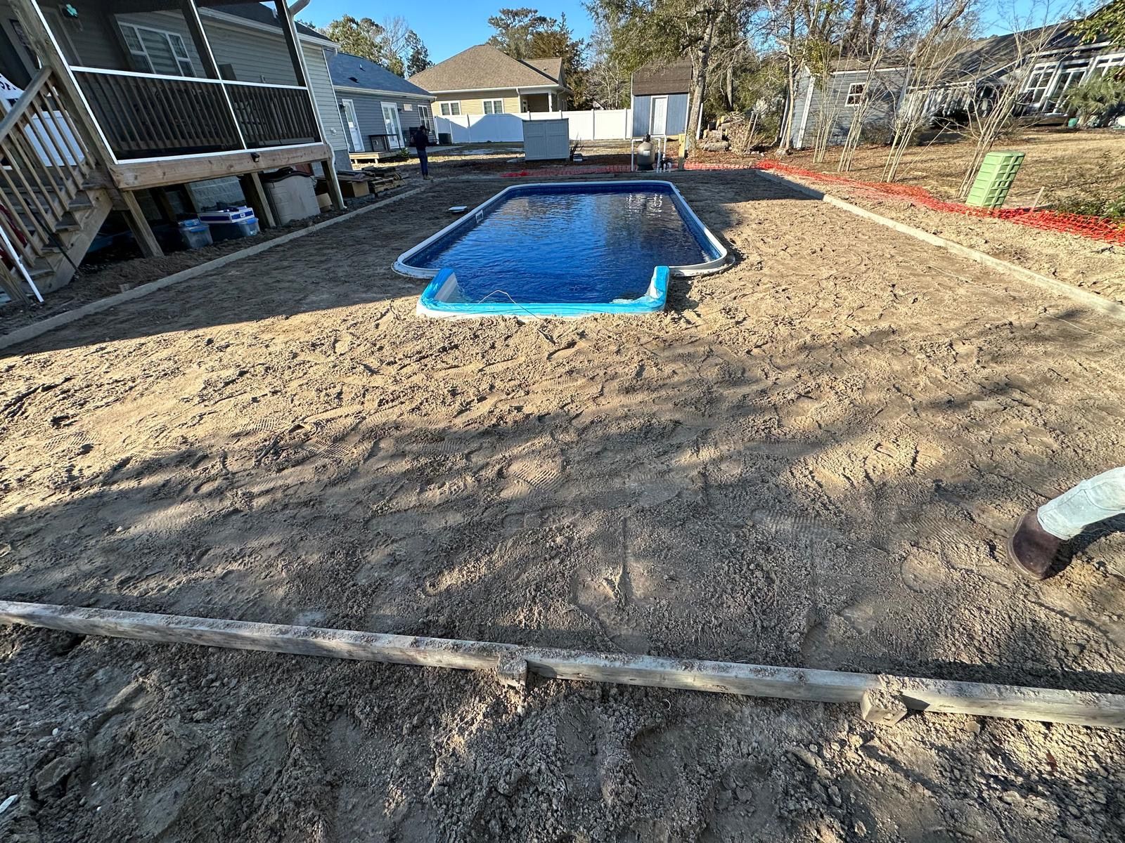 Backyard with a blue-lined in-ground pool and bare dirt yard near a house