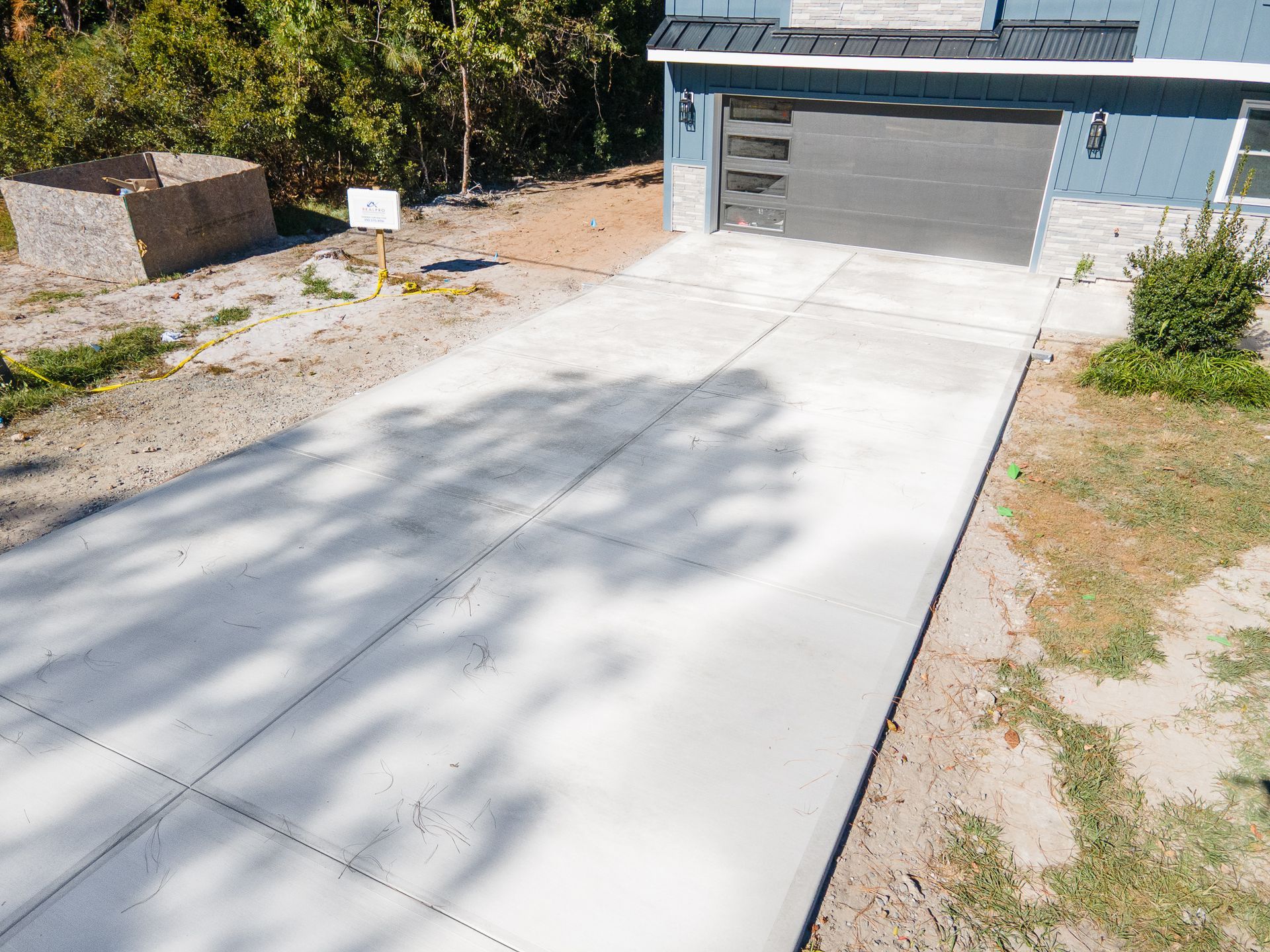 Concrete driveway leading to a closed garage with a small sign and shrubs beside it