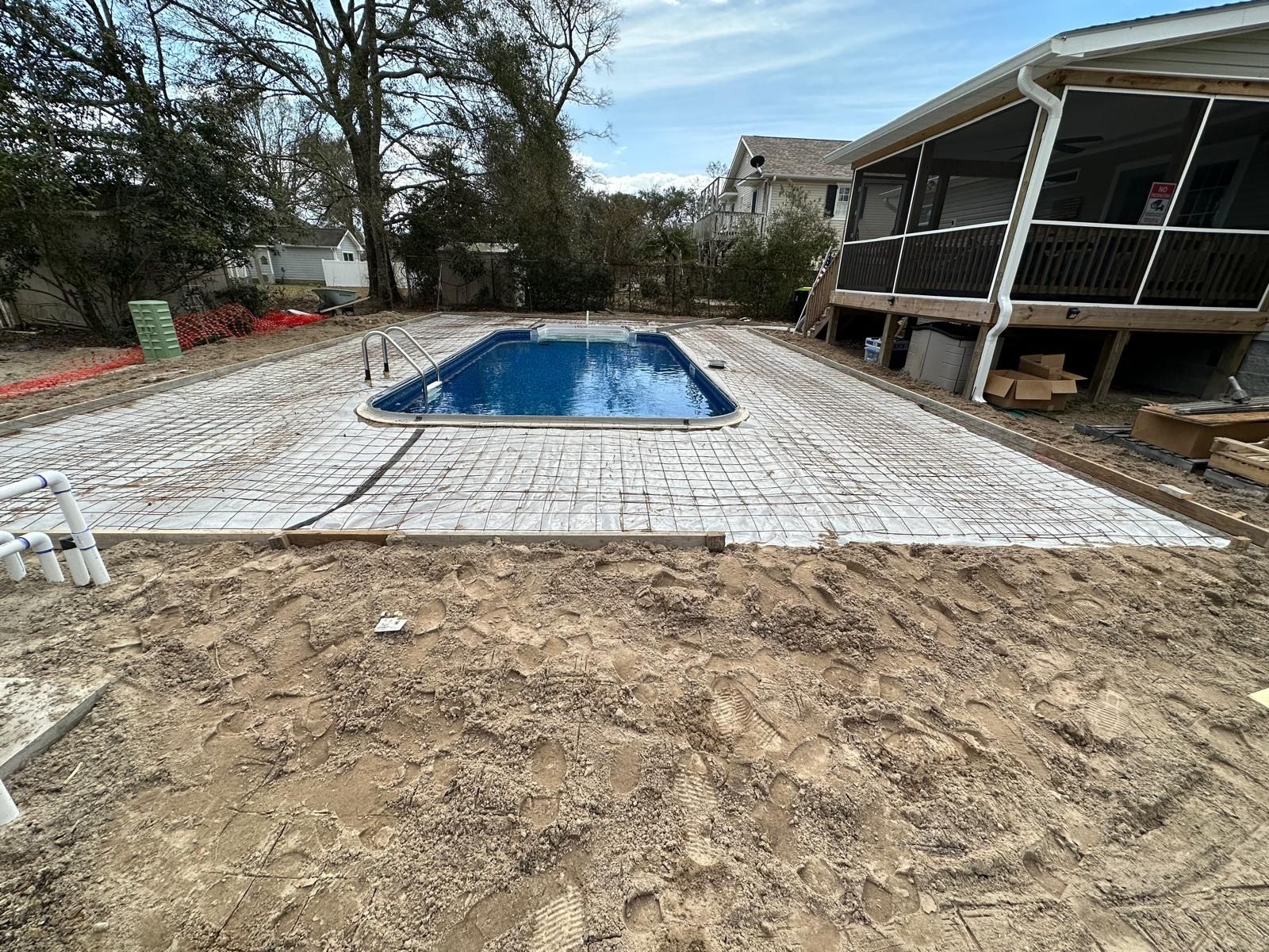 Backyard with a blue rectangular pool set in a paved patio beside a covered porch and bare dirt foreground