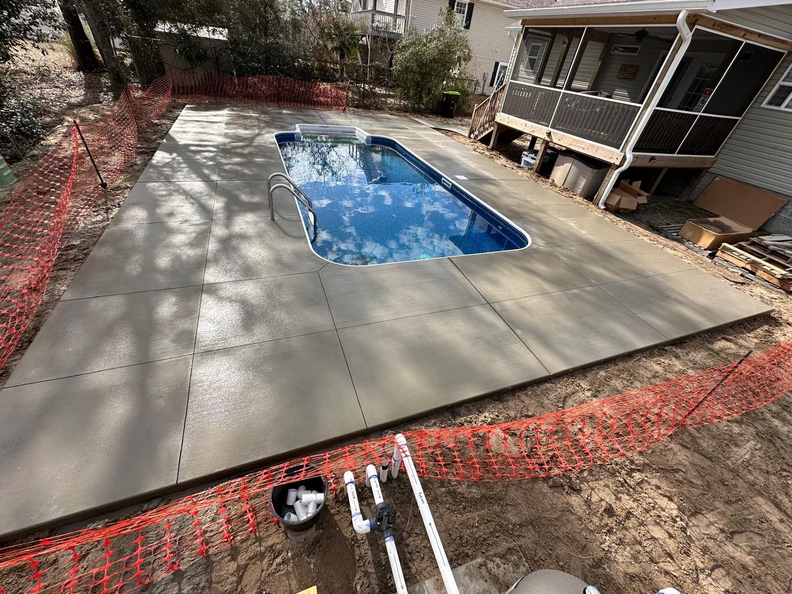 Backyard swimming pool with blue water, surrounded by a concrete patio and house porch.