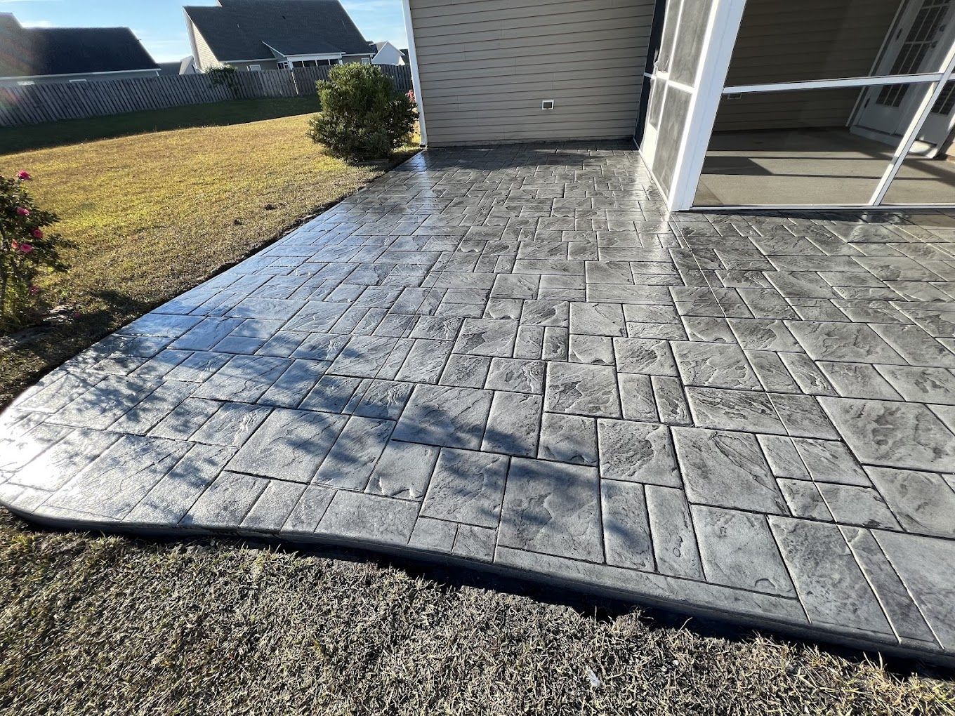Stamped concrete patio beside a garage, with a white railing and a small grassy yard.