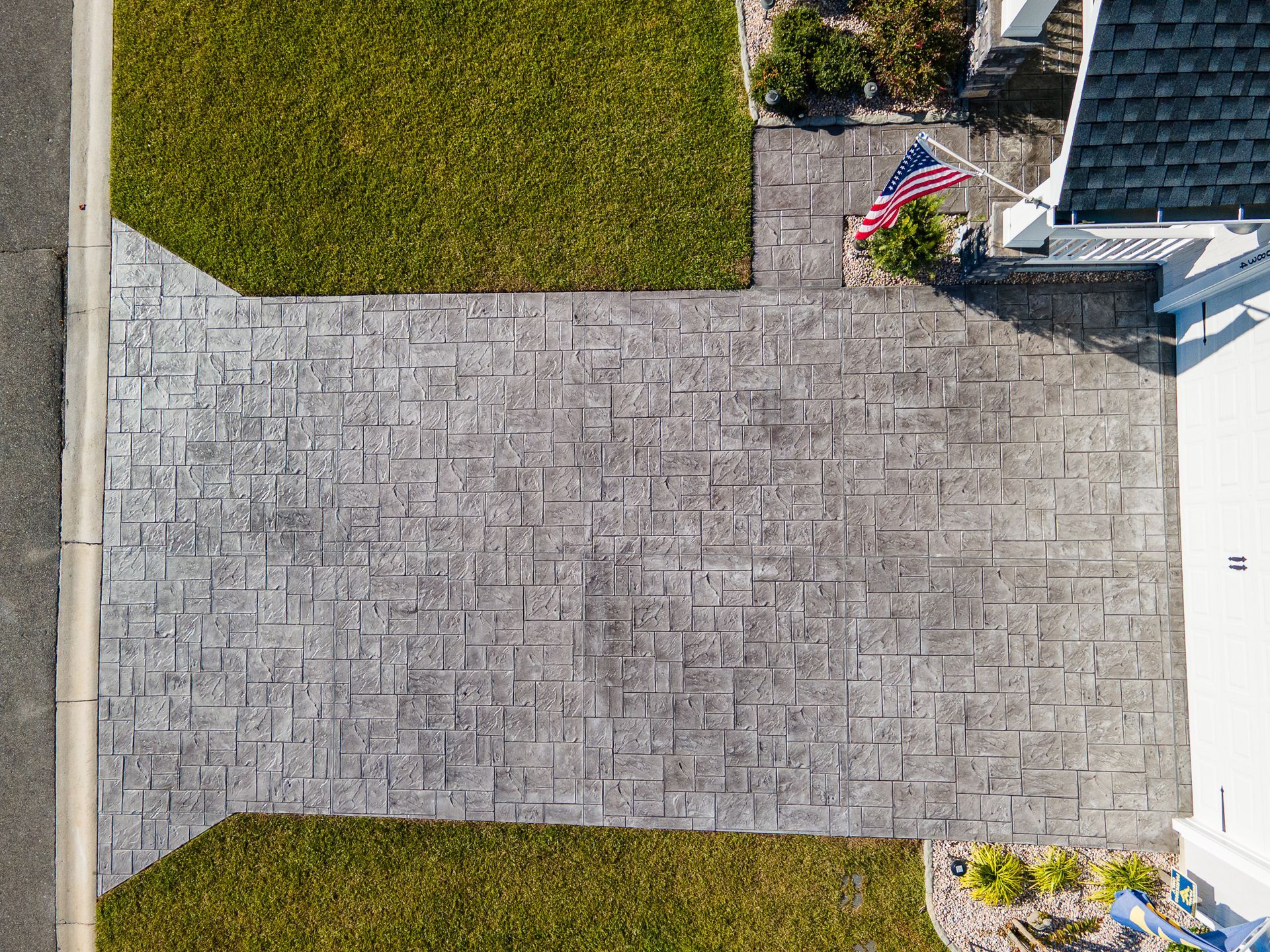 Overhead view of a stone driveway between green lawns and a patio with a small American flag.