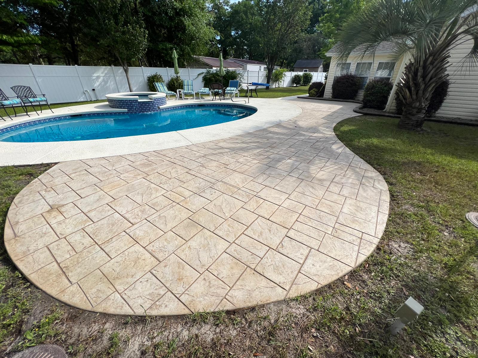 Curved stone patio beside a blue swimming pool in a landscaped backyard
