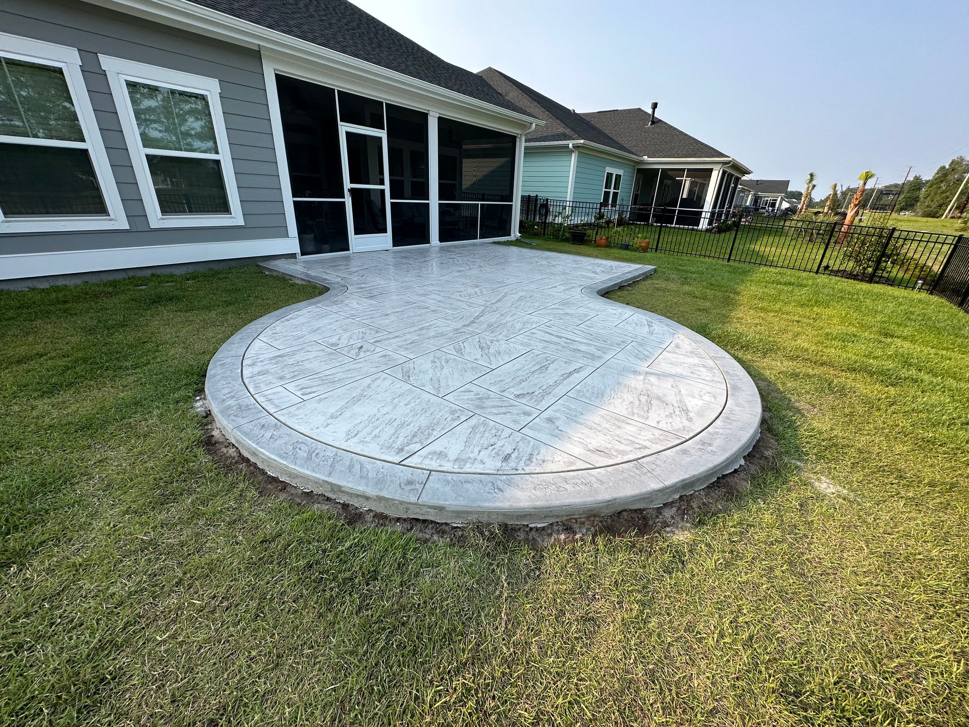 Backyard patio with a curved concrete slab beside a house and green lawn