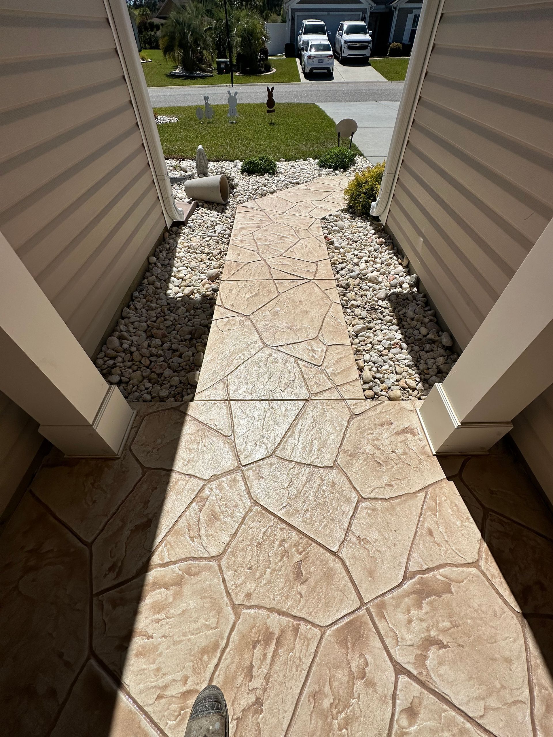 Narrow stone walkway leading from a porch to a small landscaped front yard and driveway.