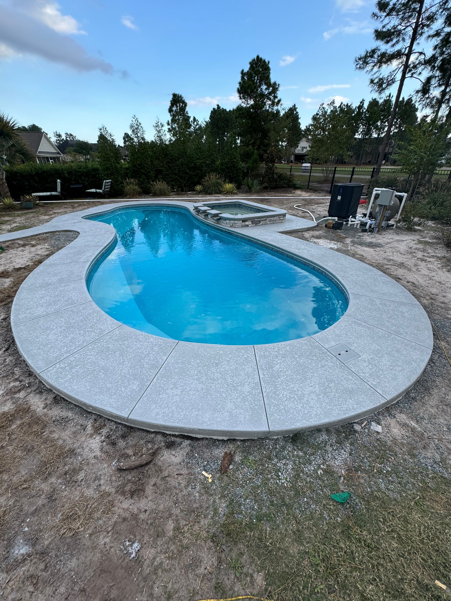 Round backyard swimming pool with blue water, white coping, and trees in the background