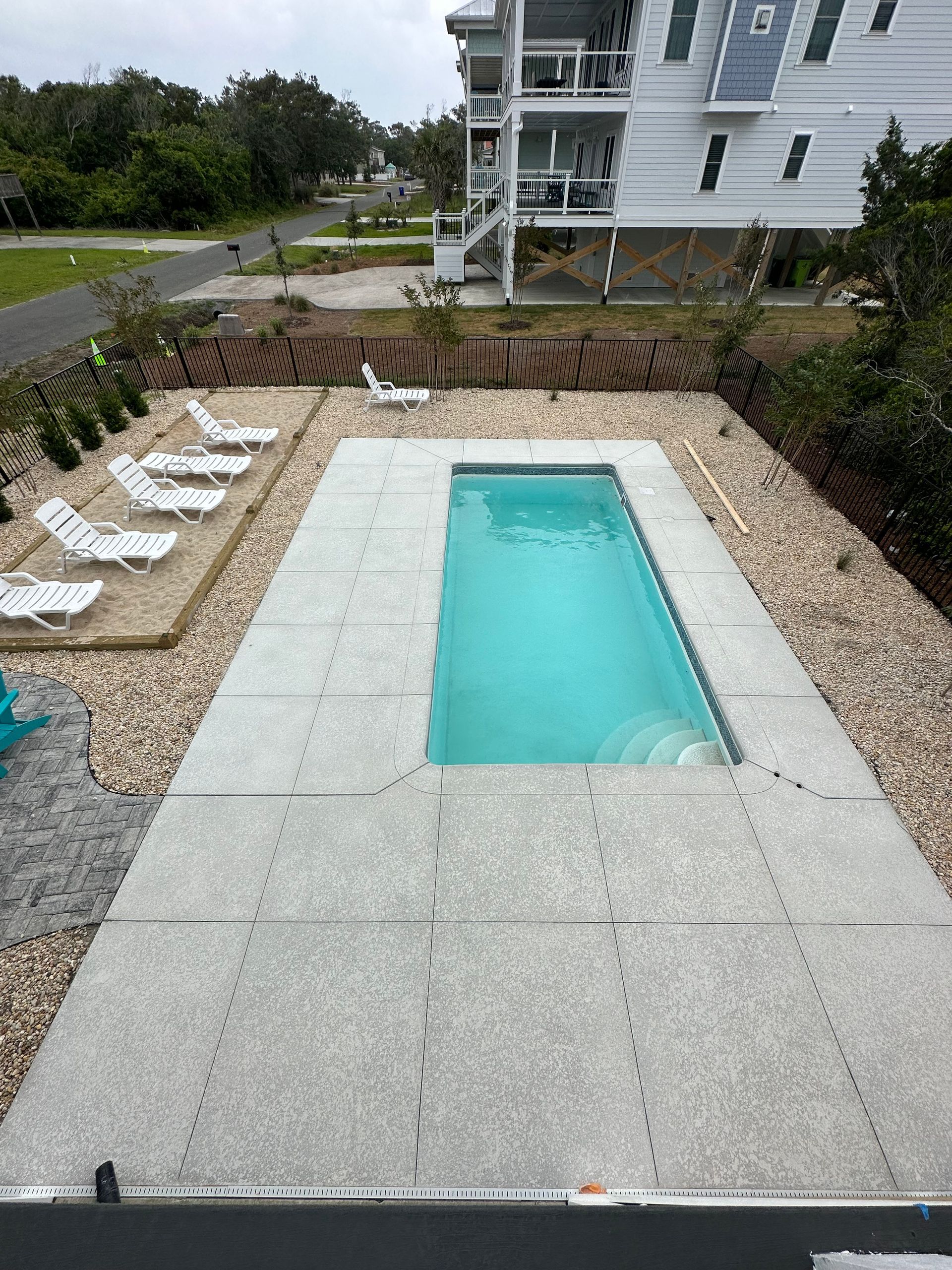 Backyard with a rectangular in-ground pool surrounded by white stone and lounge chairs