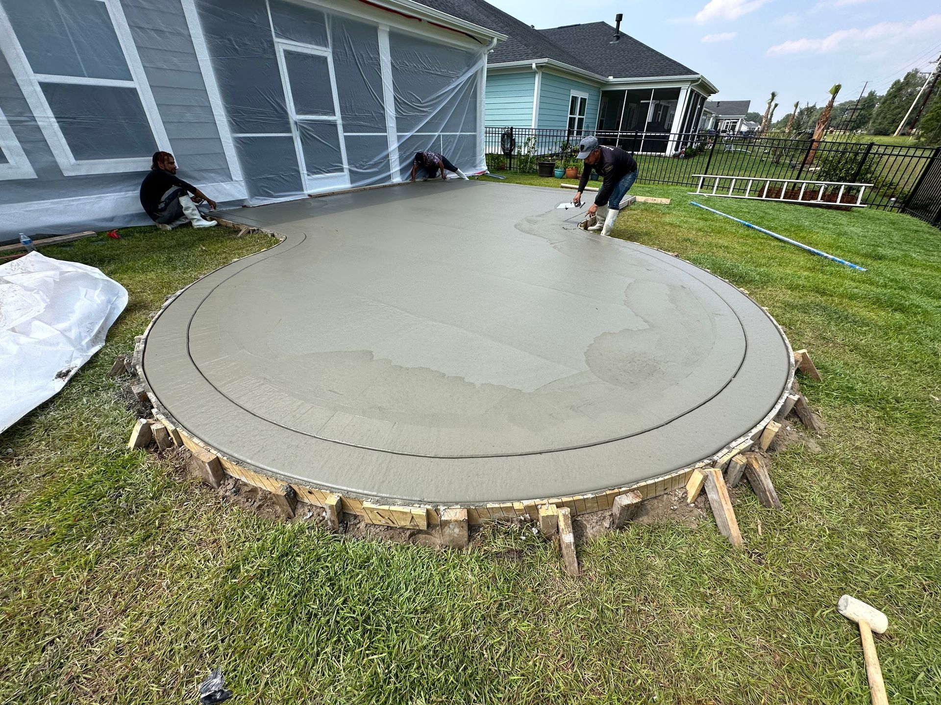 Workers smoothing a circular concrete patio beside a house, with stone edging and grass around it